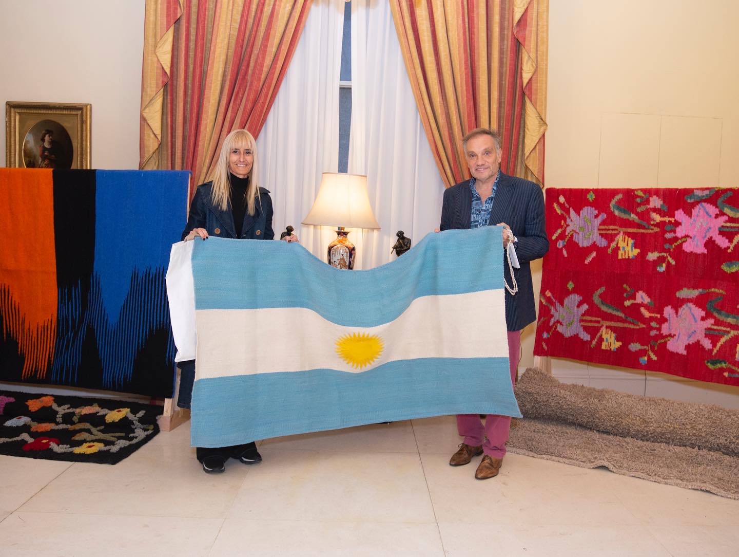 Carolina Pavetto junto al embajador argentino Javier Figueroa, con una de las banderas argentinas tejidas a mano, durante su visita a Londres, que coincidió con la muerte de la Reina Isabel II