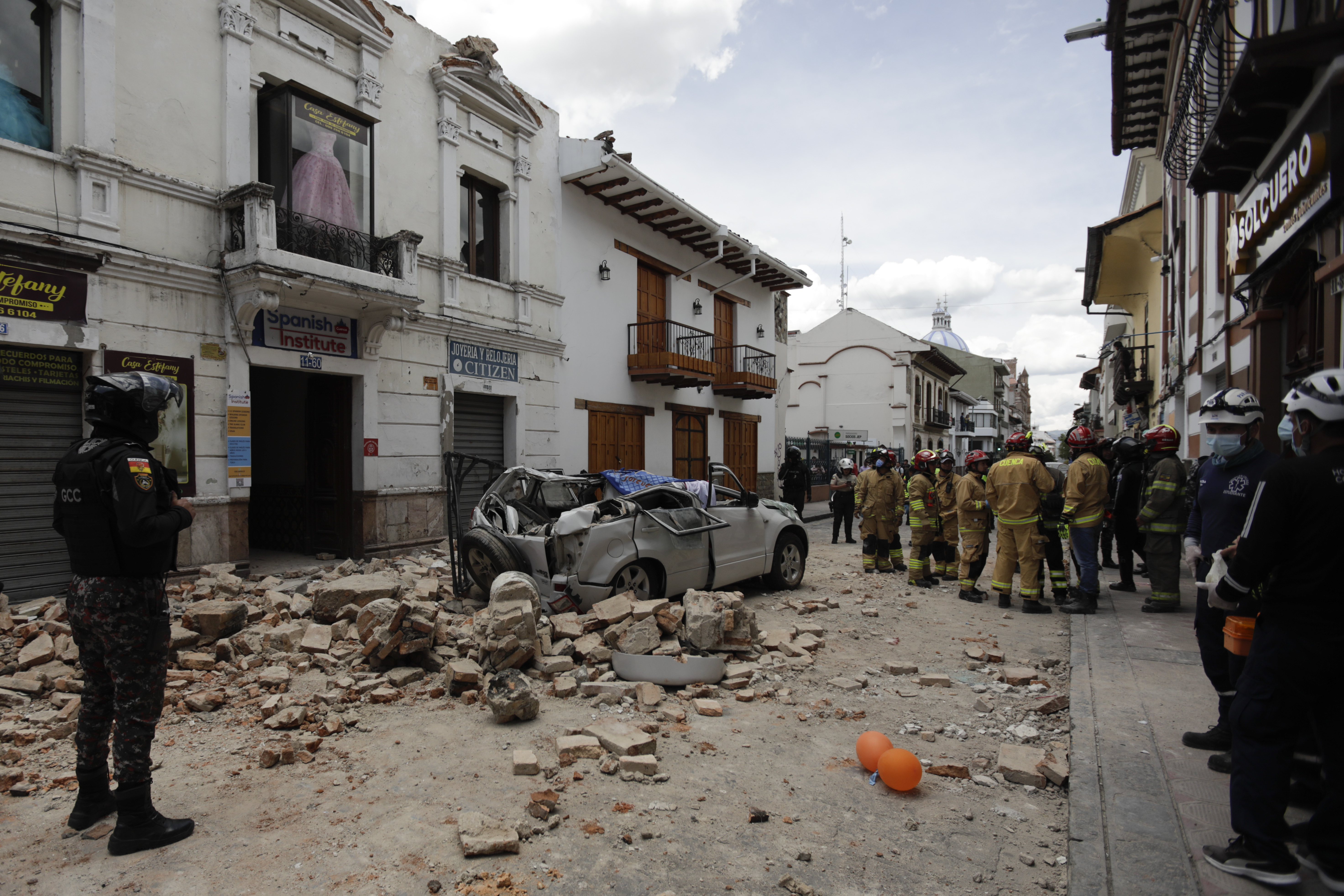 Rescuers stand next to a car crushed by debris from an earthquake, in Cuenca, Ecuador, Saturday, March 18, 2023. The US Geological Survey reported the magnitude 6.7 quake about 50 miles south of Guayaquil.  (AP Photo/Xavier Caivinagua)