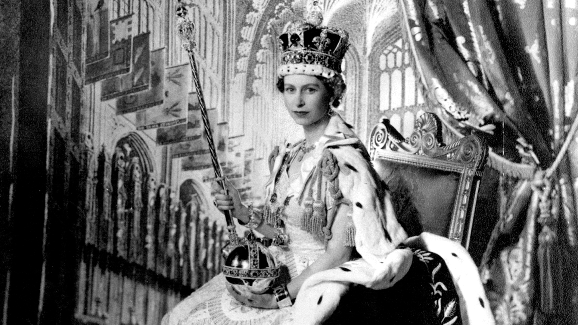 La reina Isabel II. En el Salón del Trono del Palacio de Buckingham tras su coronación: S.M. la Reina Isabel II posó para esta fotografía realizada por Cecil Beaton, en el Salón del Trono del Palacio de Buckingham tras su Coronación el 2 de junio de 1953. Está vestida con su traje de Coronación y su túnica de terciopelo púrpura. Sobre su cabeza lleva la Corona Imperial de Estado. En su mano izquierda lleva el Orbe y en la derecha el Cetro con Cruz. En sus muñecas lleva los Brazaletes de la Sinceridad. (The Grosby Group)