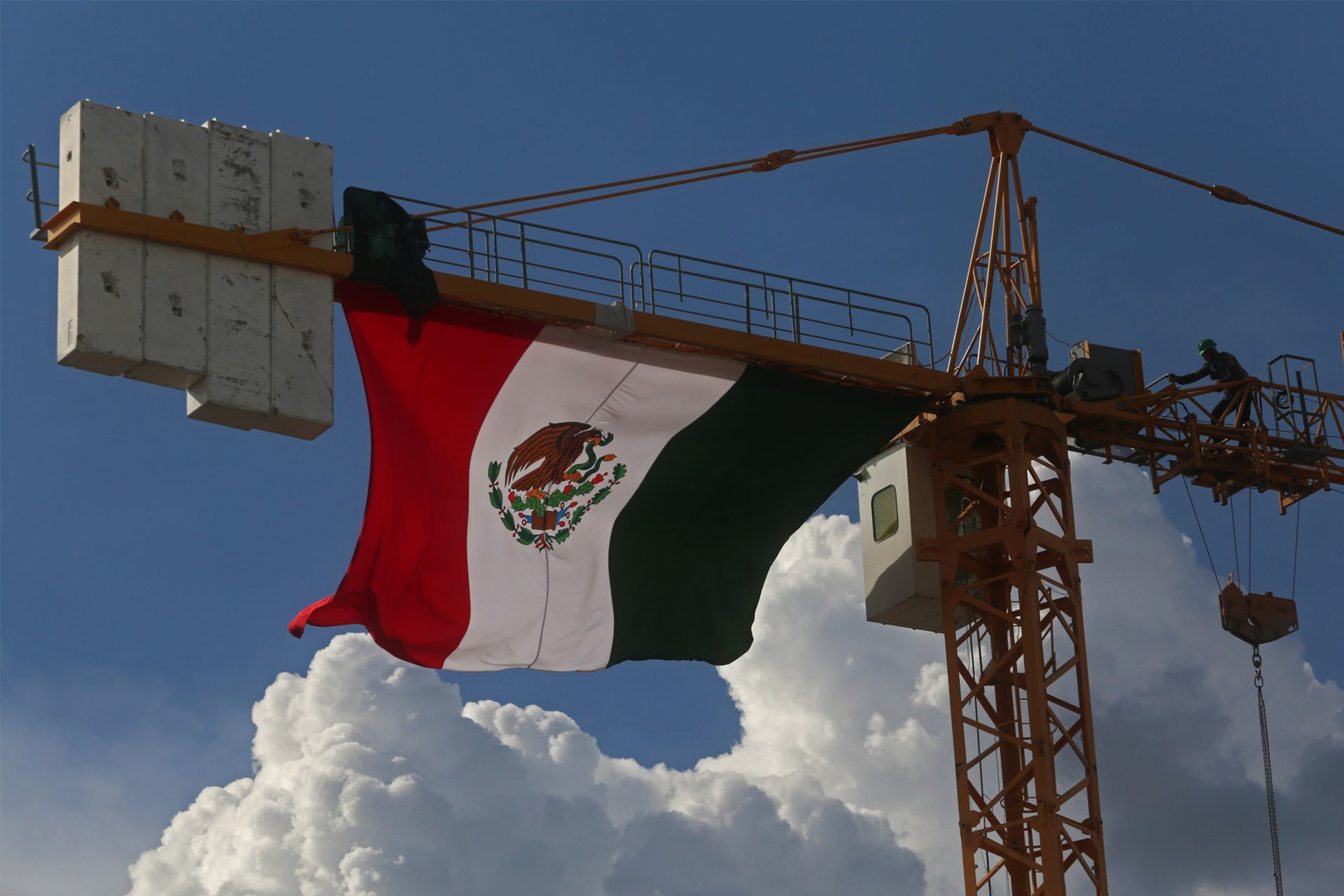Un trabajador de una obra que se realiza en avenida Hidalgo y Calzada Federalismo realiza algunas actividades cotidianas de trabajo arriba de una grúa donde se ondea la bandera nacional Mexicana.