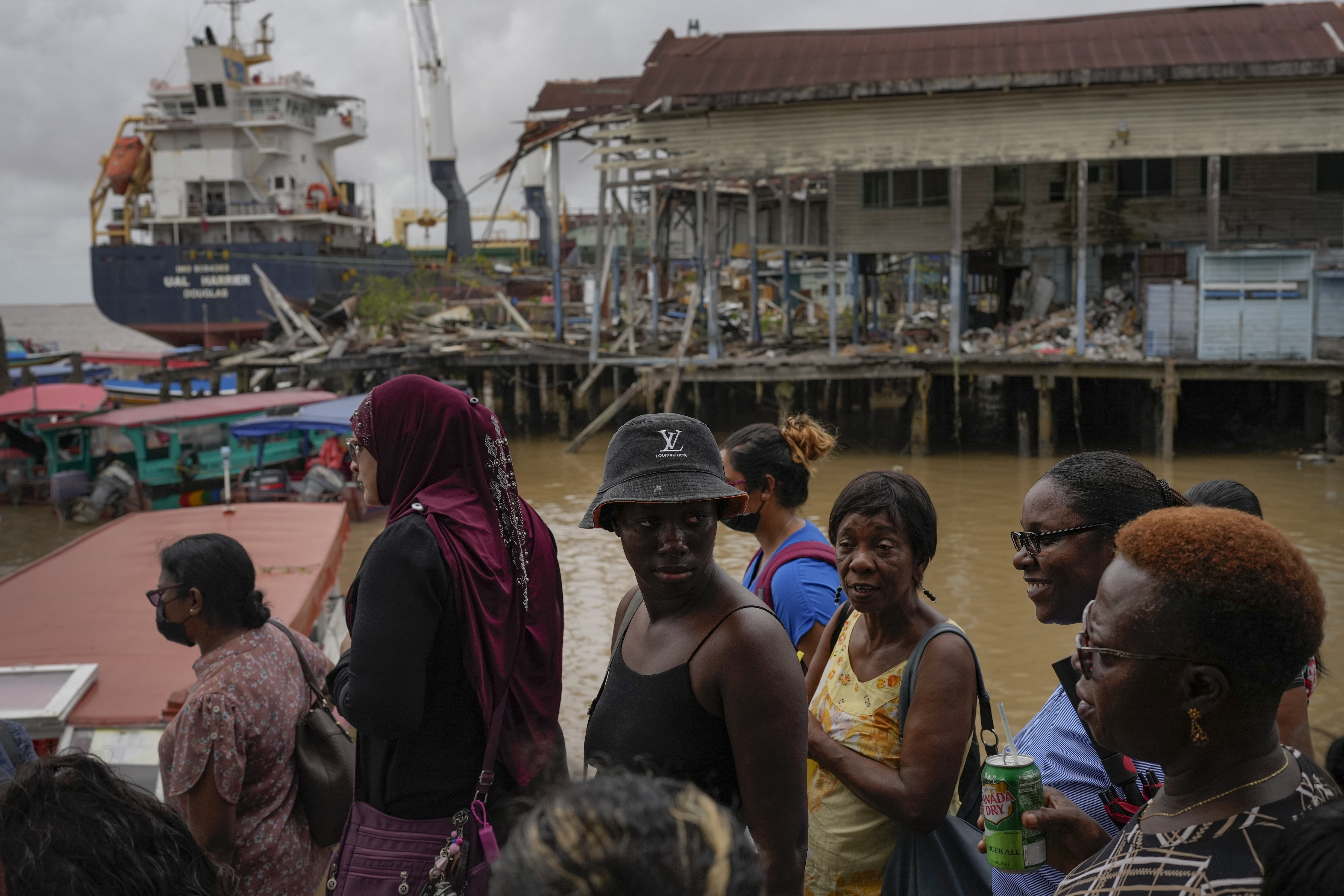 A group of people wait at the Stabroek market to cross to the other side of the Demerara River, near a merchant ship, in Georgetown, Guyana, on April 12, 2023. Guyana is on track to become the world's fourth largest oil producer in high seas, ahead of Qatar, the United States, Mexico and Norway.  (AP Photo/Matias Delacroix)