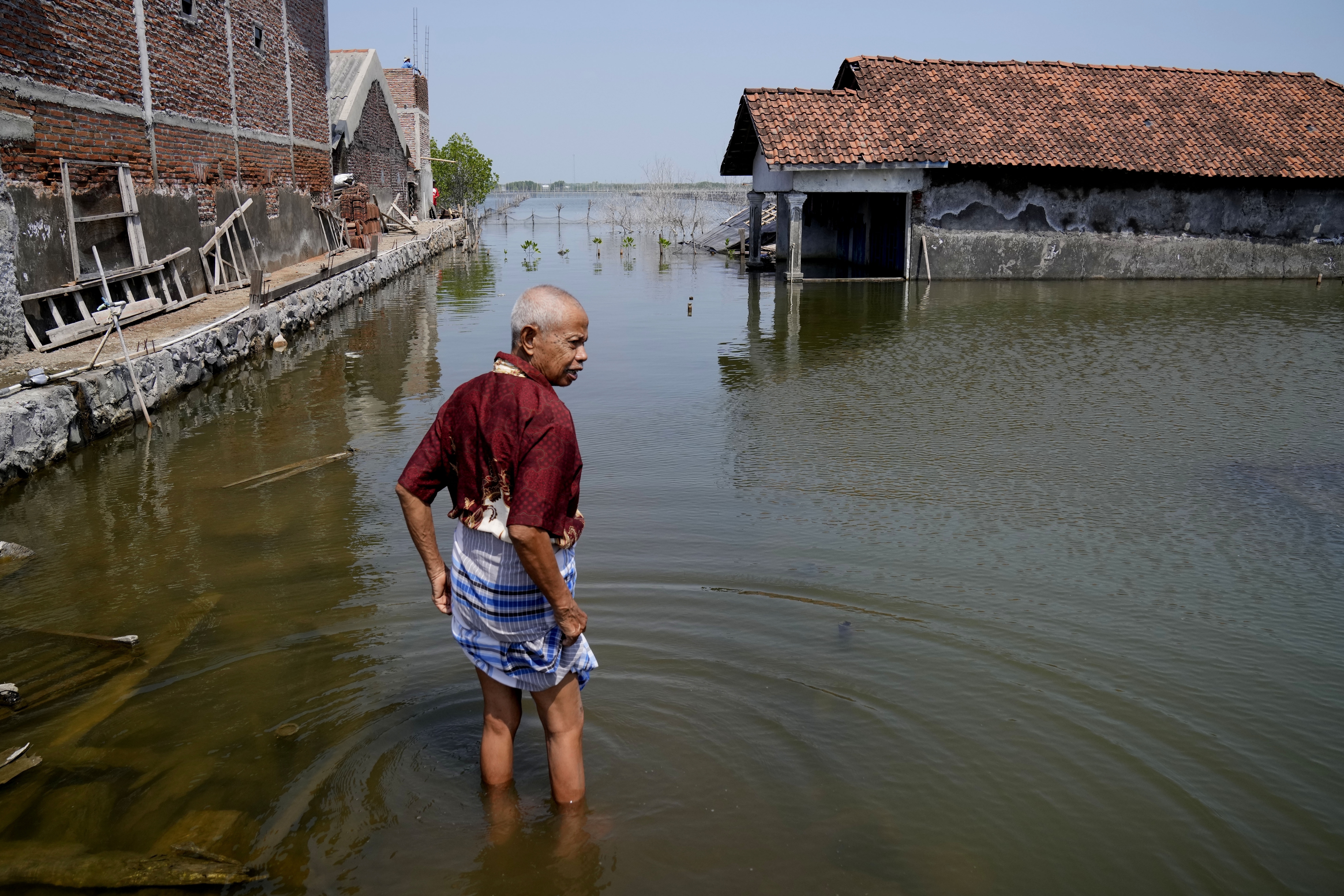 ARCHIVO - Sukarman camina por un camino inundado fuera de su casa el 30 de julio de 2022 en Timbulsloko, Java Central, Indonesia. (AP FOto/Dita Alangkara, Archivo)