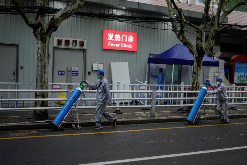 Dos trabajadores llevan bombonas de oxígeno frente a un hospital en Shanghai (REUTERS/Aly Song)