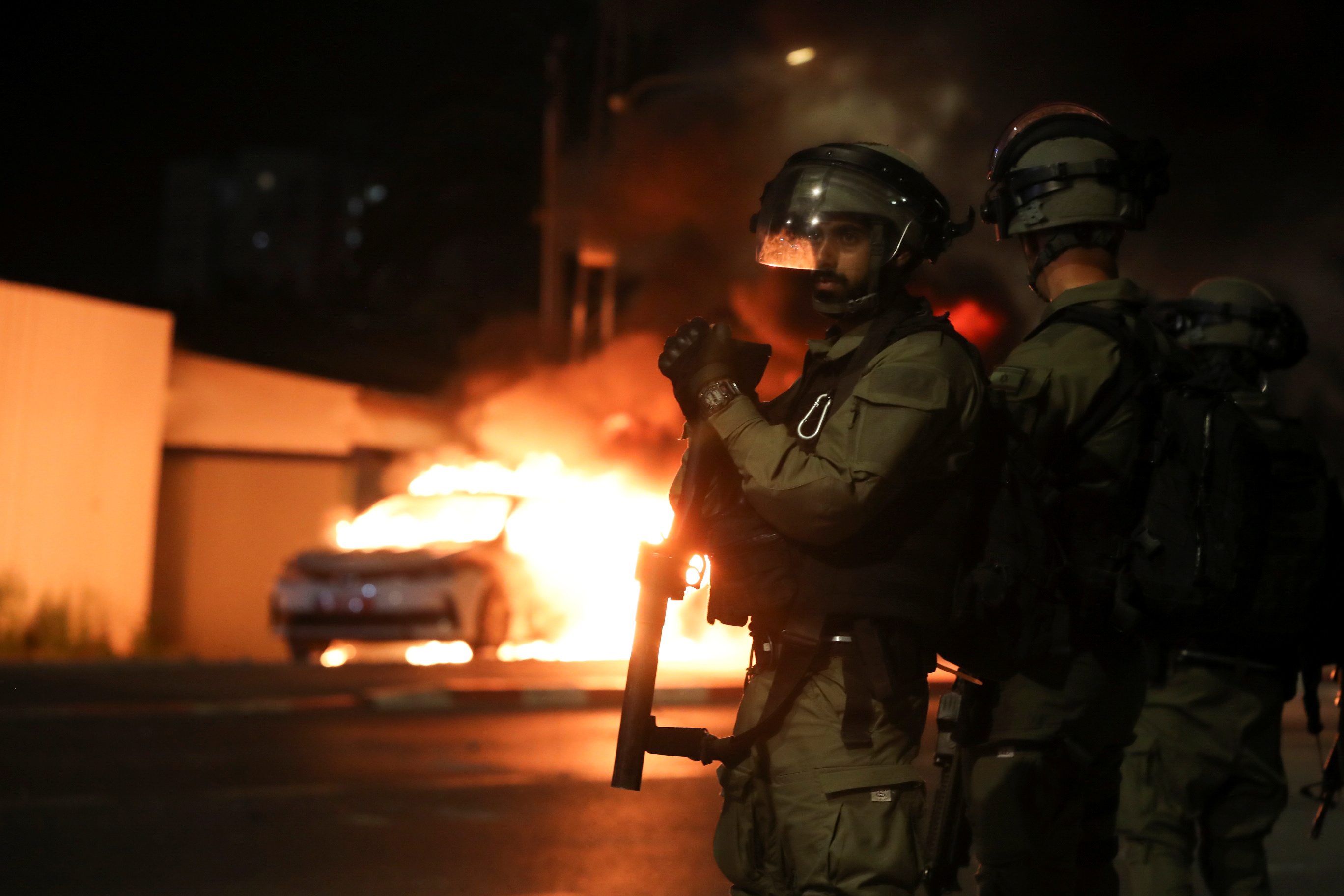 Miembros de las fuerzas de seguridad israelíes permanecen cerca de un coche de policía israelí en llamas durante los enfrentamientos entre la policía israelí y miembros de la minoría árabe del país en la ciudad árabe-judía de Lod, Israel 12 de mayo de 2021. REUTERS/Ammar Awad