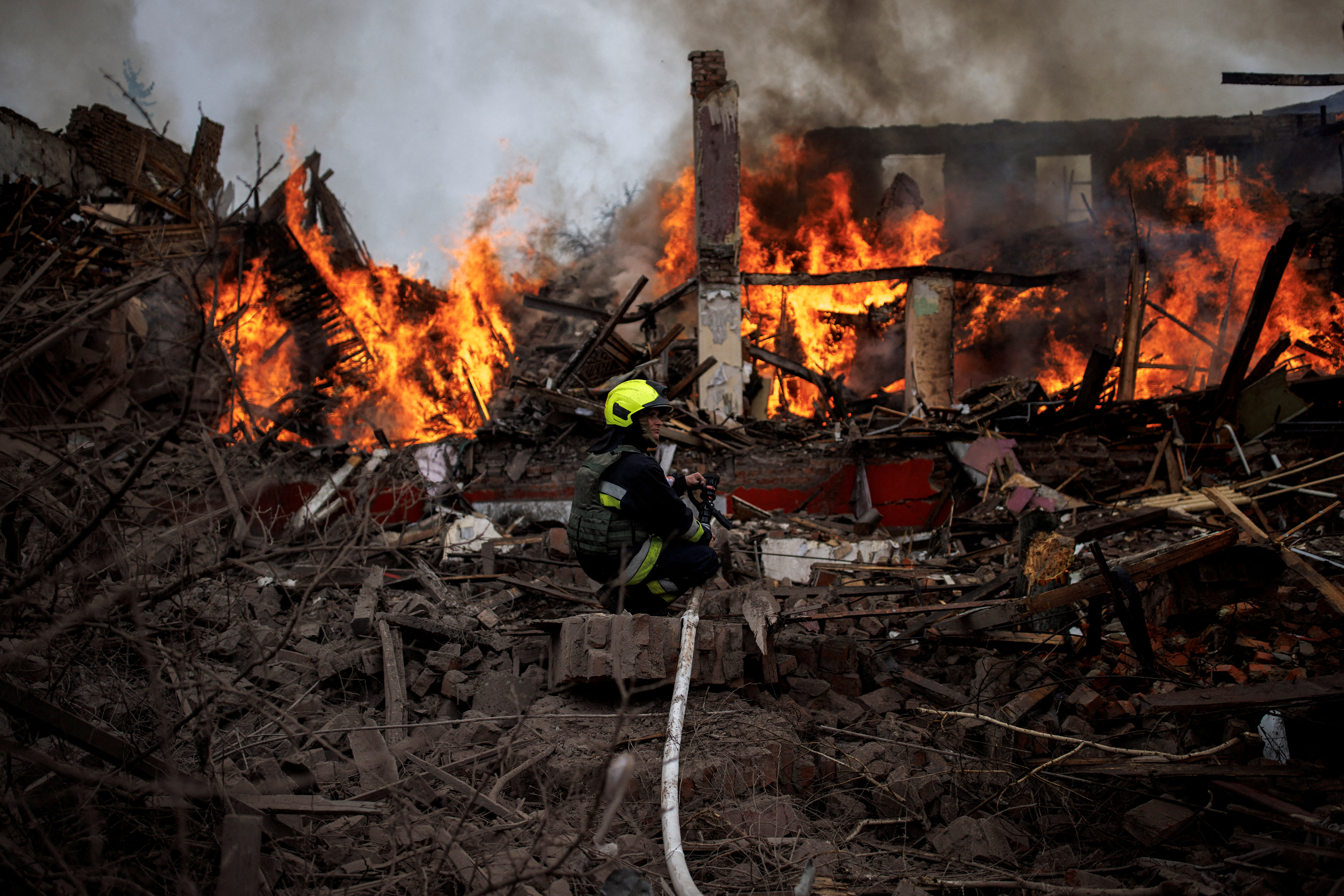 Un bombero sostiene una manguera junto a un edificio en llamas, luego de un ataque con misiles cerca del Aeropuerto Internacional de Kharkiv el 12 de abril de 2022 (REUTERS/Alkis Konstantinidis)