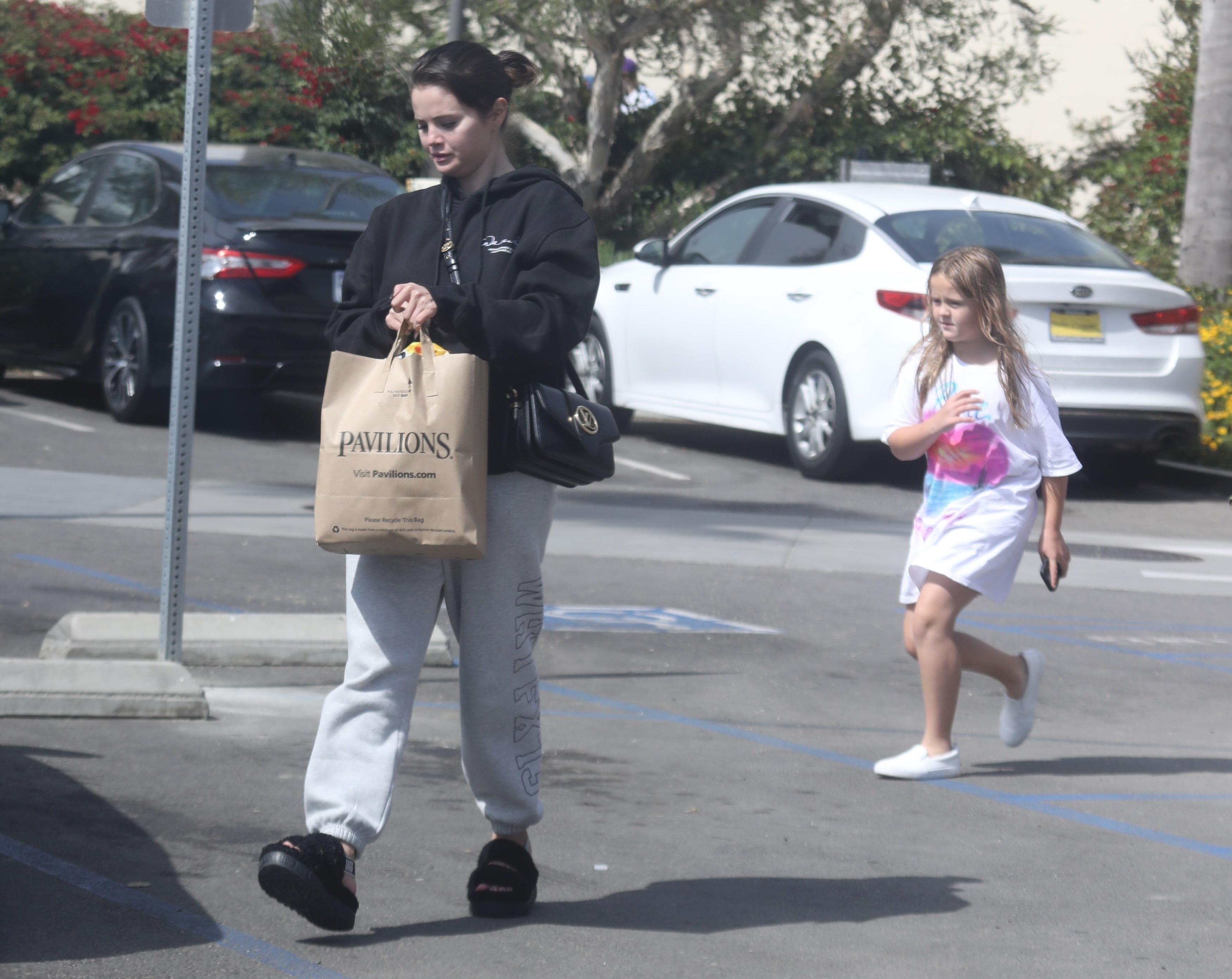 Selena Gomez was photographed in the parking lot of a supermarket in Malibu, where she went to do the daily shopping accompanied by her younger sister.  The artist wore a comfortable look: gray jogging pants, faux leather sandals and a black jumpsuit