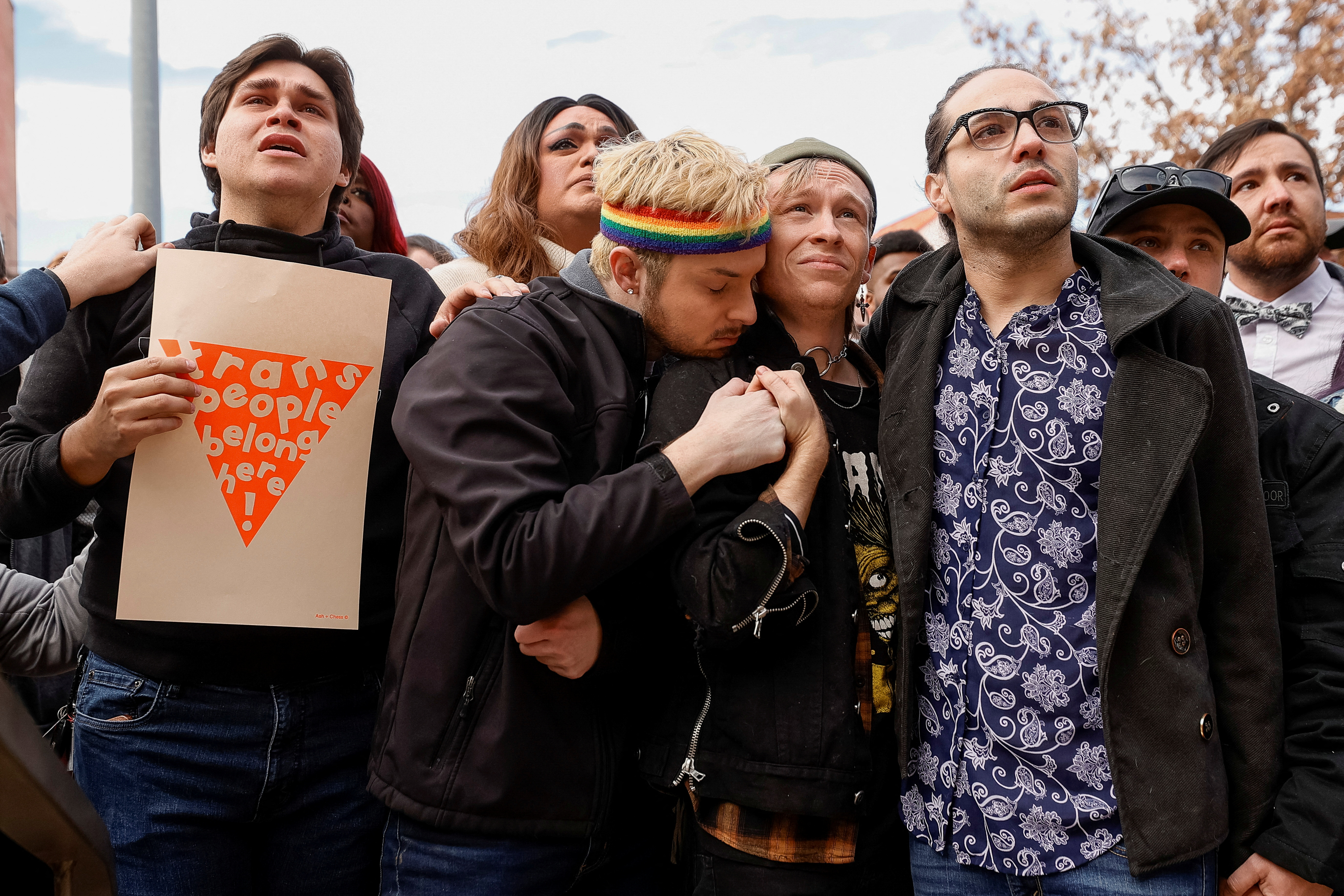 Carter Rodriguez holds a sign in support of trans people as Michael Anderson embraces Wyatt Kent and Autumn Quinn looks on during an unfurling ceremony of the "Sacred Cloth" Pride Flag at City Hall after a mass shooting at LGBTQ nightclub Club Q in Colorado Springs, Colorado, U.S. November 23, 2022. Anderson is bartender at the club and Kent's partner, Daniel David Aston, was killed in the attack. REUTERS/Isaiah J. Downing