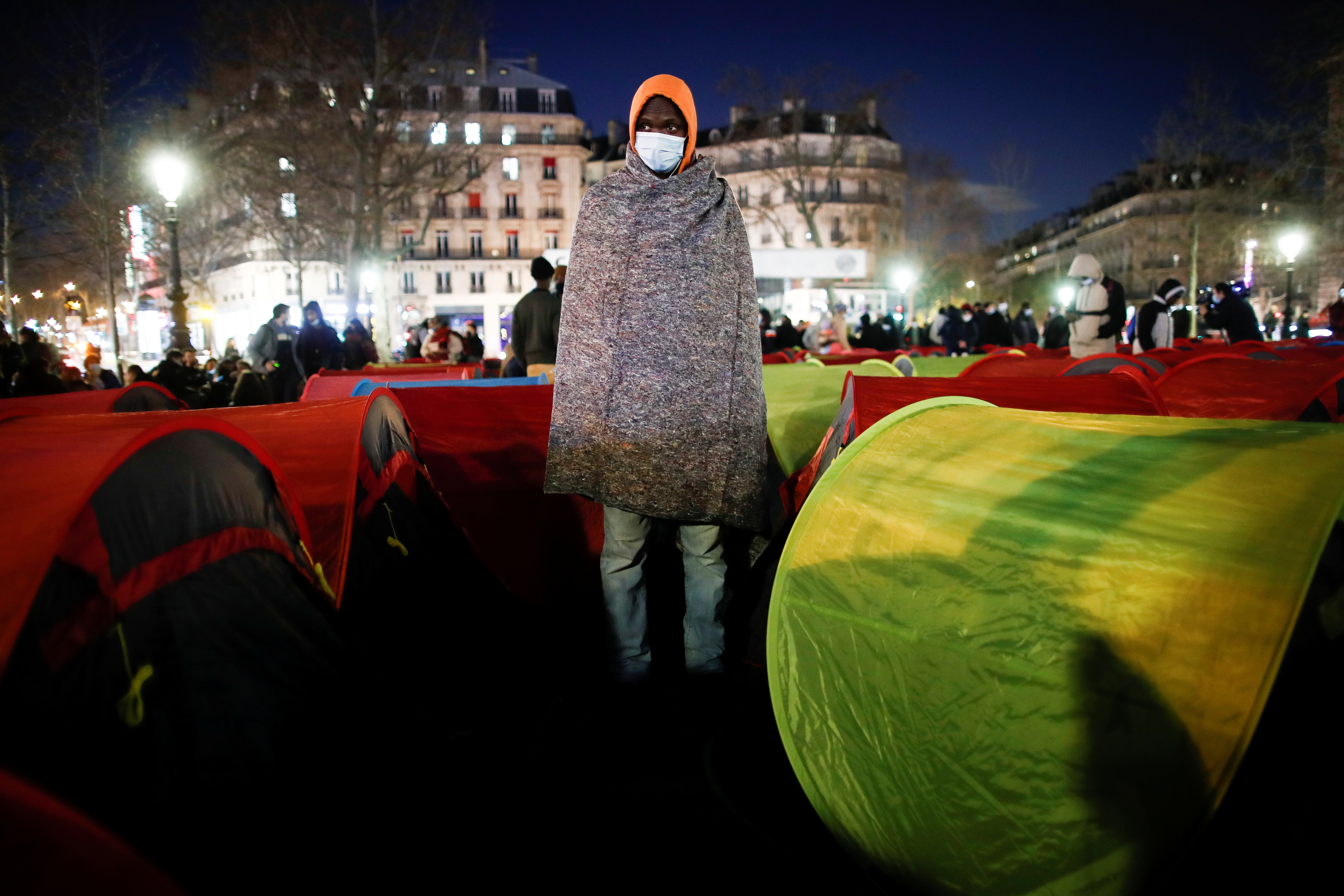 Un hombre se encuentra entre las tiendas de campaña colocadas por migrantes en la plaza de la República para el inicio de una "Noche de la Solidaridad" para llamar la atención sobre sus condiciones de vida y exigir alojamiento en París, el 25 de marzo de 2021 (REUTERS/Benoit Tessier)