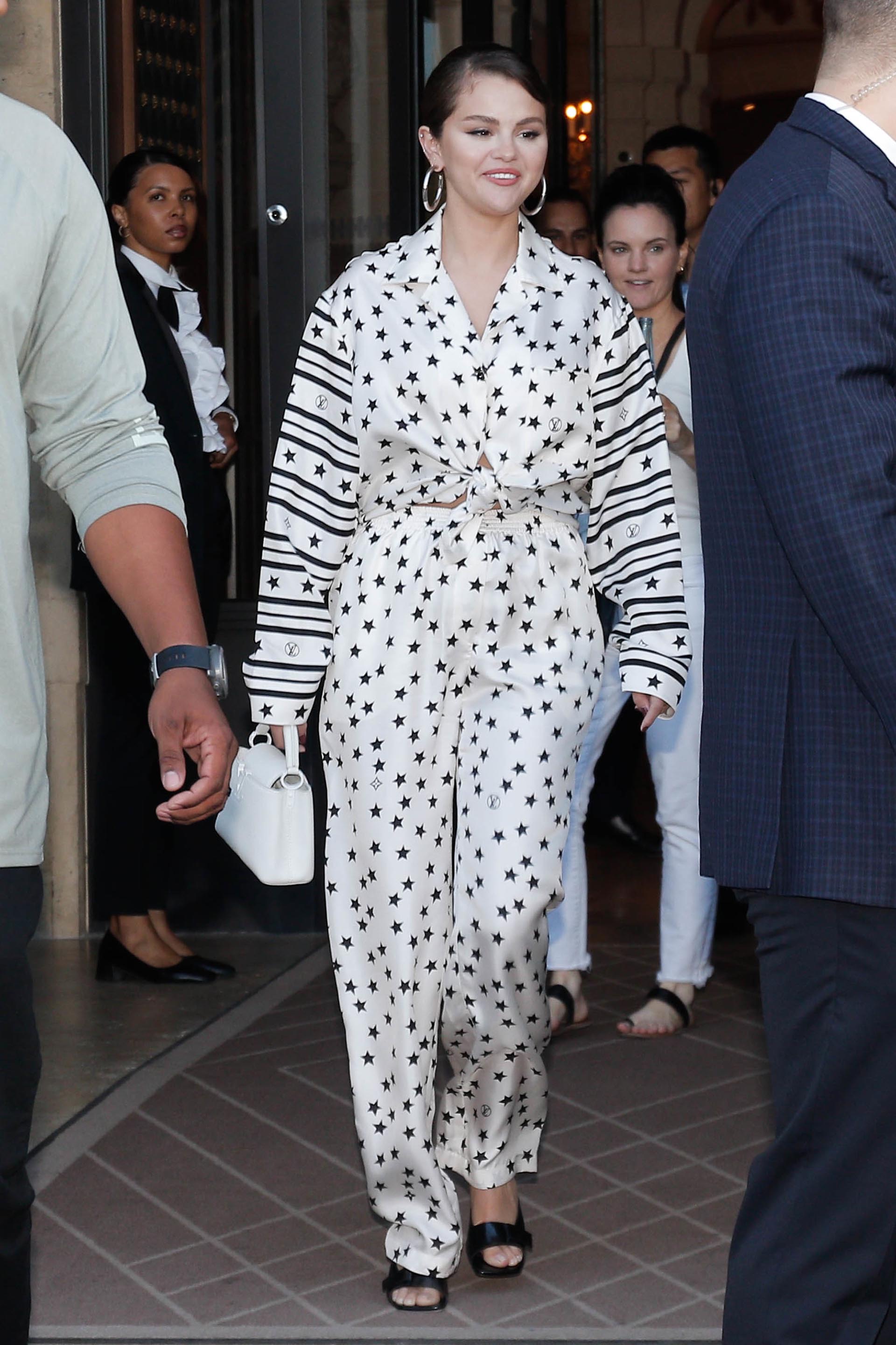 Selena Gomez fue fotografiada cuando salía del hotel en el que se hospeda durante sus días en París. Asistió a un evento de moda y marcó tendencia con su look: un conjunto de pantalón y camisa de satén blanco estampado con estrellas y en sus mangas tenía líneas negras
