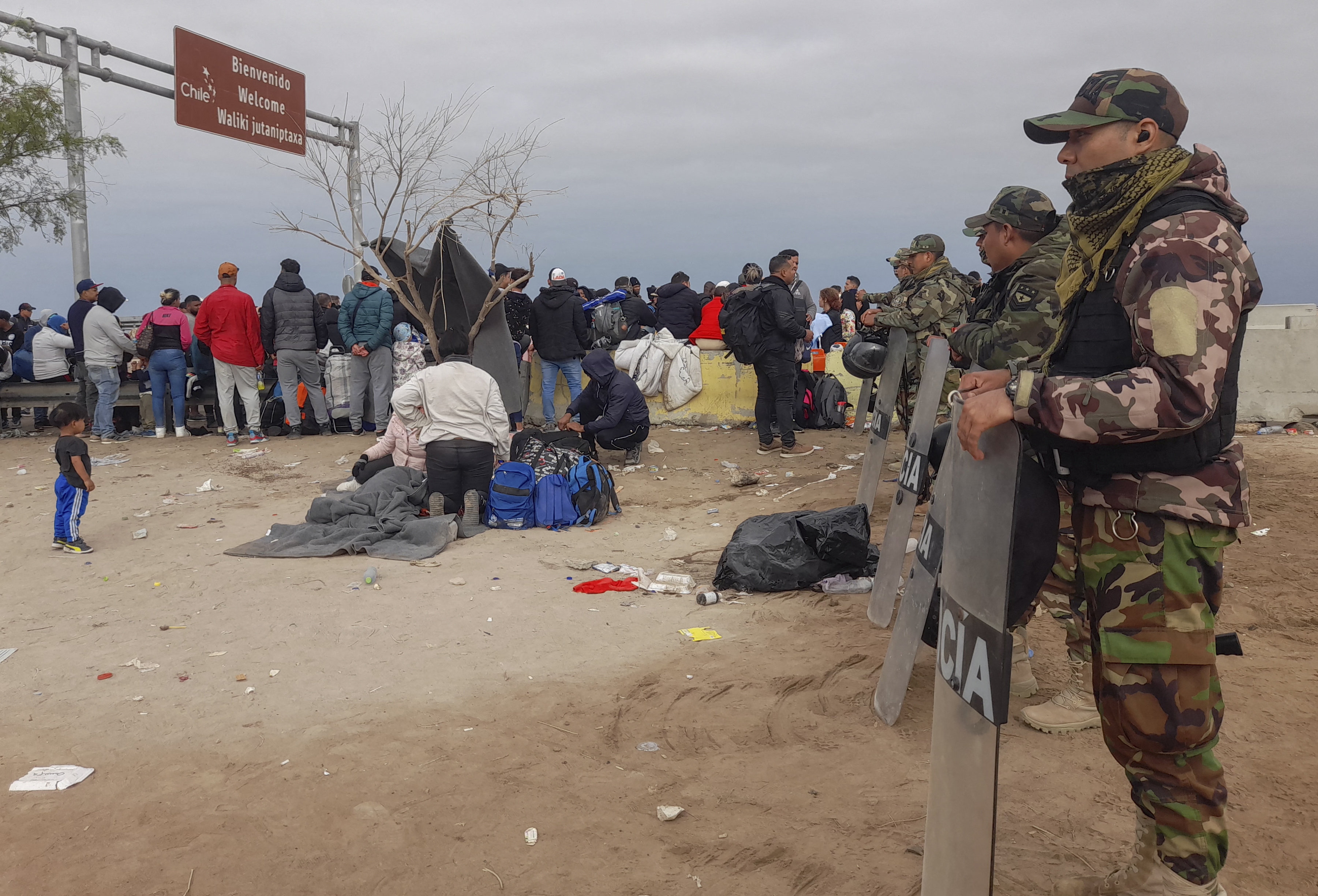 Policías peruanos montan guardia en un campamento de migrantes de varias nacionalidades que permanecen varados en un desierto en la frontera entre Perú y Chile, el 26 de abril de 2023 (Javier Rumiche / AFP)