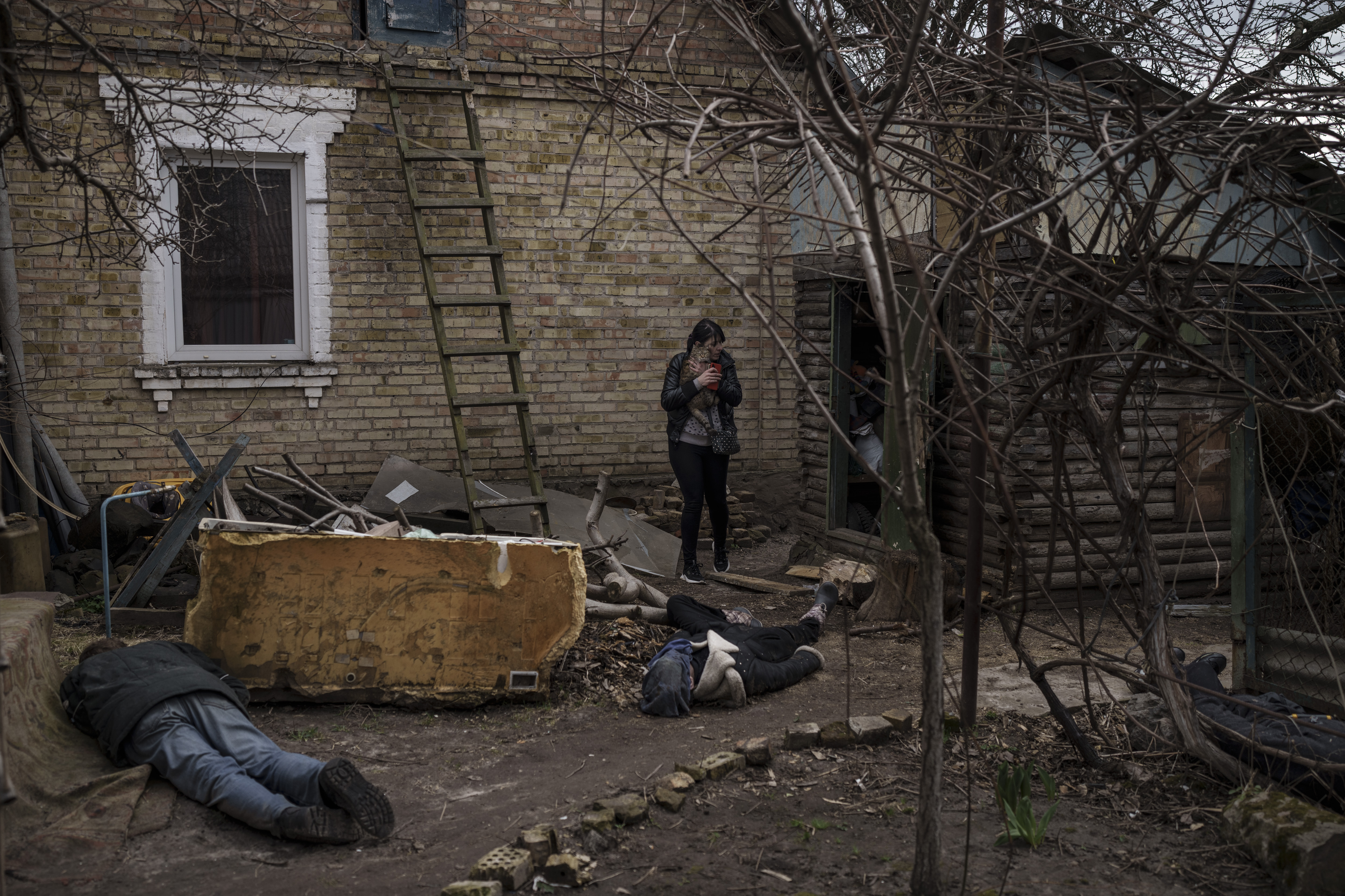 Ira Gavriluk sostiene a su gato mientras camina entre los cuerpos de su marido, su hermano y otro hombre, que fueron asesinados fuera de su casa en Bucha, en las afueras de Kiev (AP Photo/Felipe Dana)