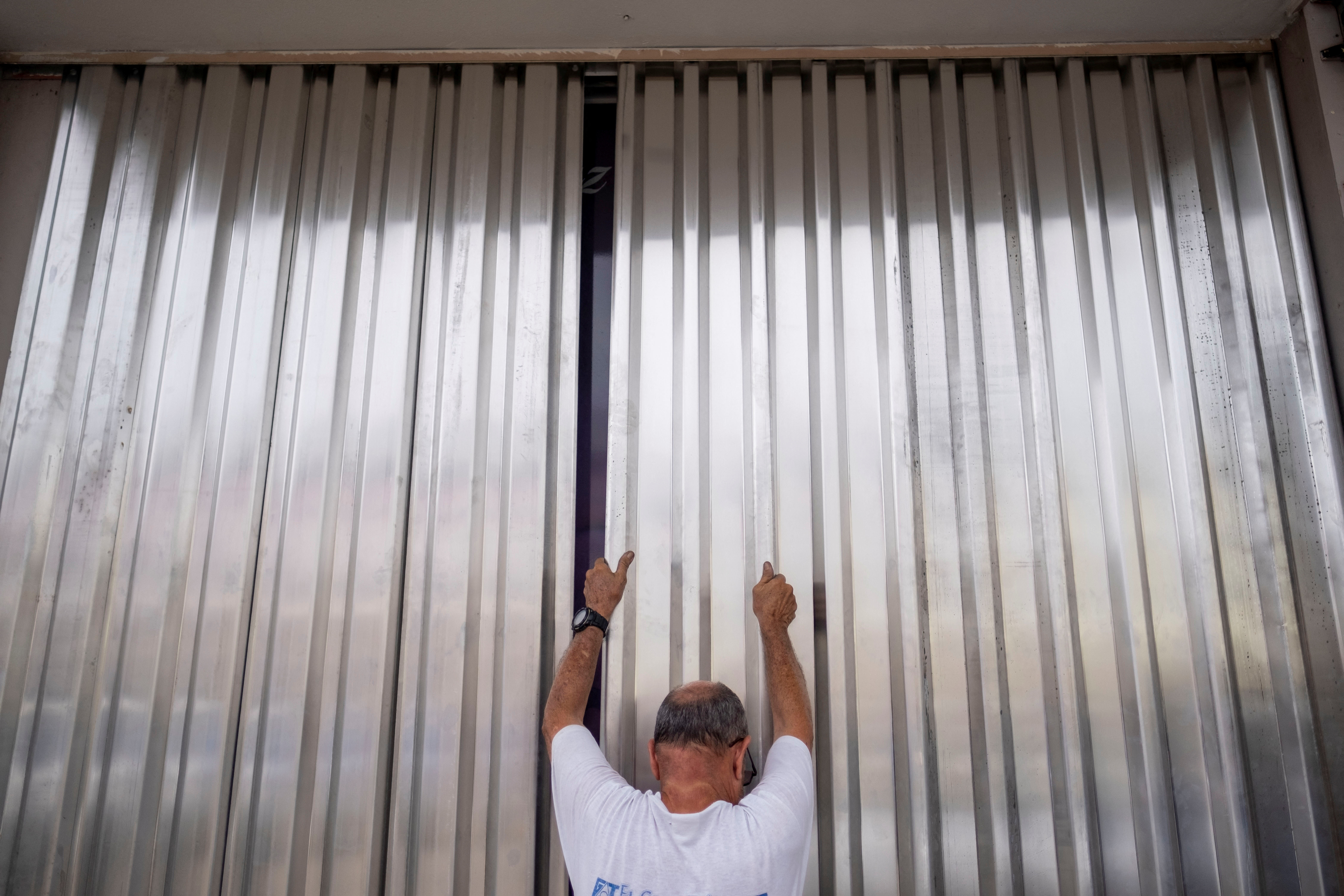 Un empleado de un consultorio dental instala persianas metálicas para tormentas en preparación para la llegada del huracán Fiona y sus fuertes lluvias en Cabo Rojo. REUTERS/Ricardo Arduengo

