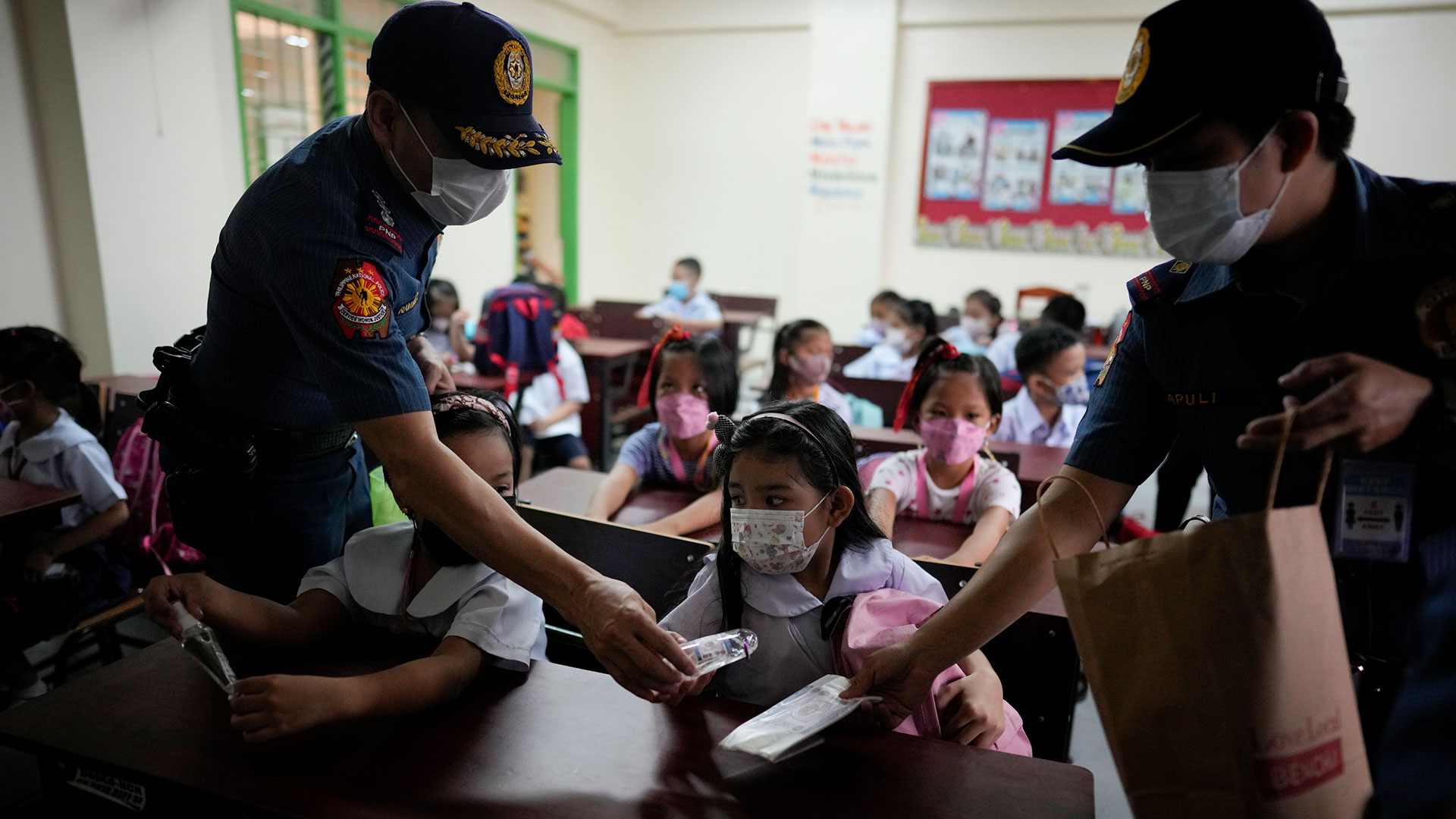 La policía distribuye alcohol y máscaras faciales a los estudiantes durante la apertura de clases en la Escuela Primaria San Juan en el área metropolitana de Manila, Filipinas, el lunes 22 de agosto de 2022.  (Foto AP/Aarón Favila)

