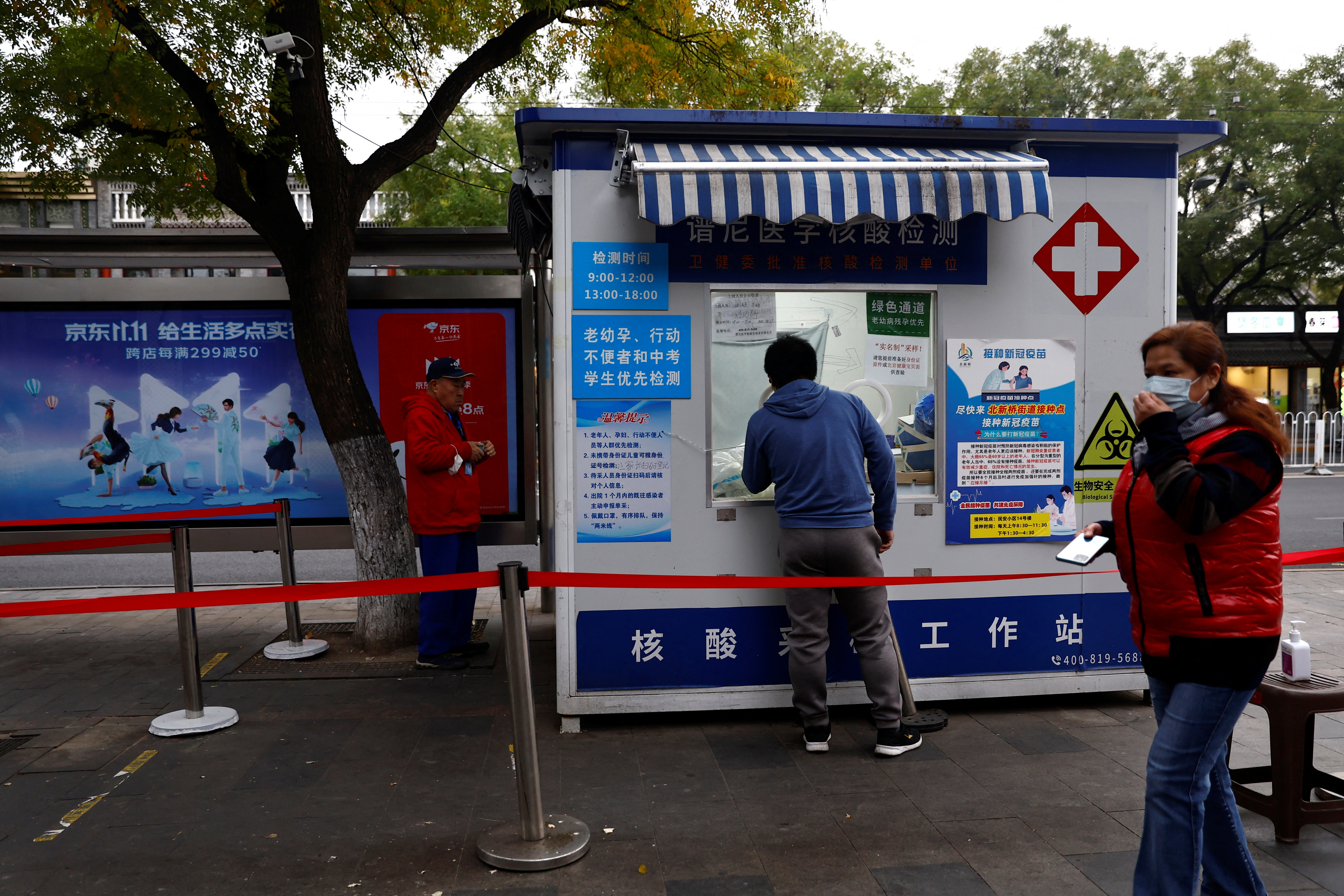 A un hombre se le toma un hisopado para una prueba de la enfermedad COVID-19 en una cabina de pruebas junto a una cartelera con publicidad para el festival de compras del día de los solteros, en Beijing, China, el 27 de octubre de 2022. REUTERS/Tingshu Wang