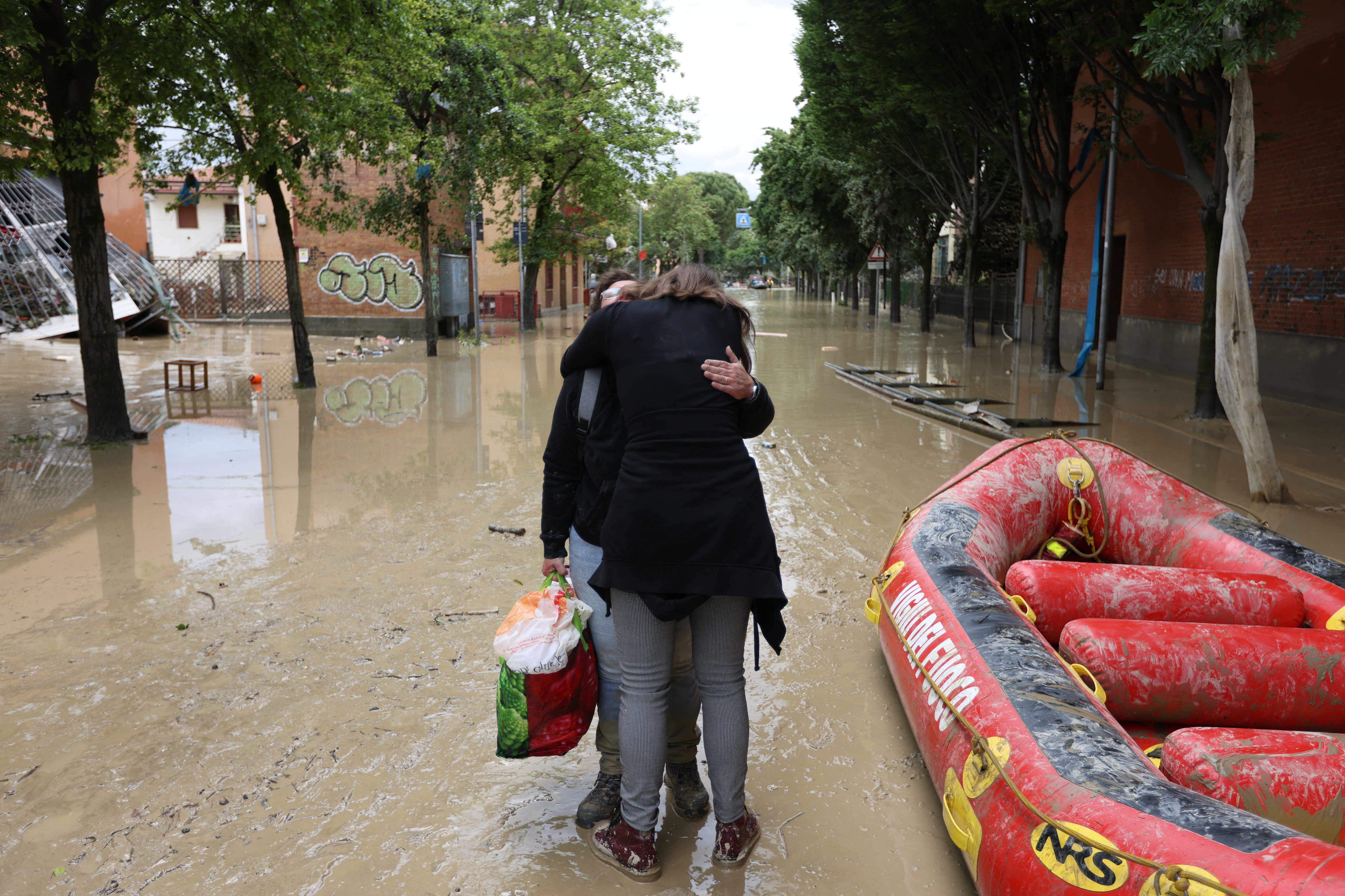 Dos personas se abrazan en una calle inundada en Faenza, Italia, el 18 de mayo de 2023 (REUTERS/Claudia Greco)