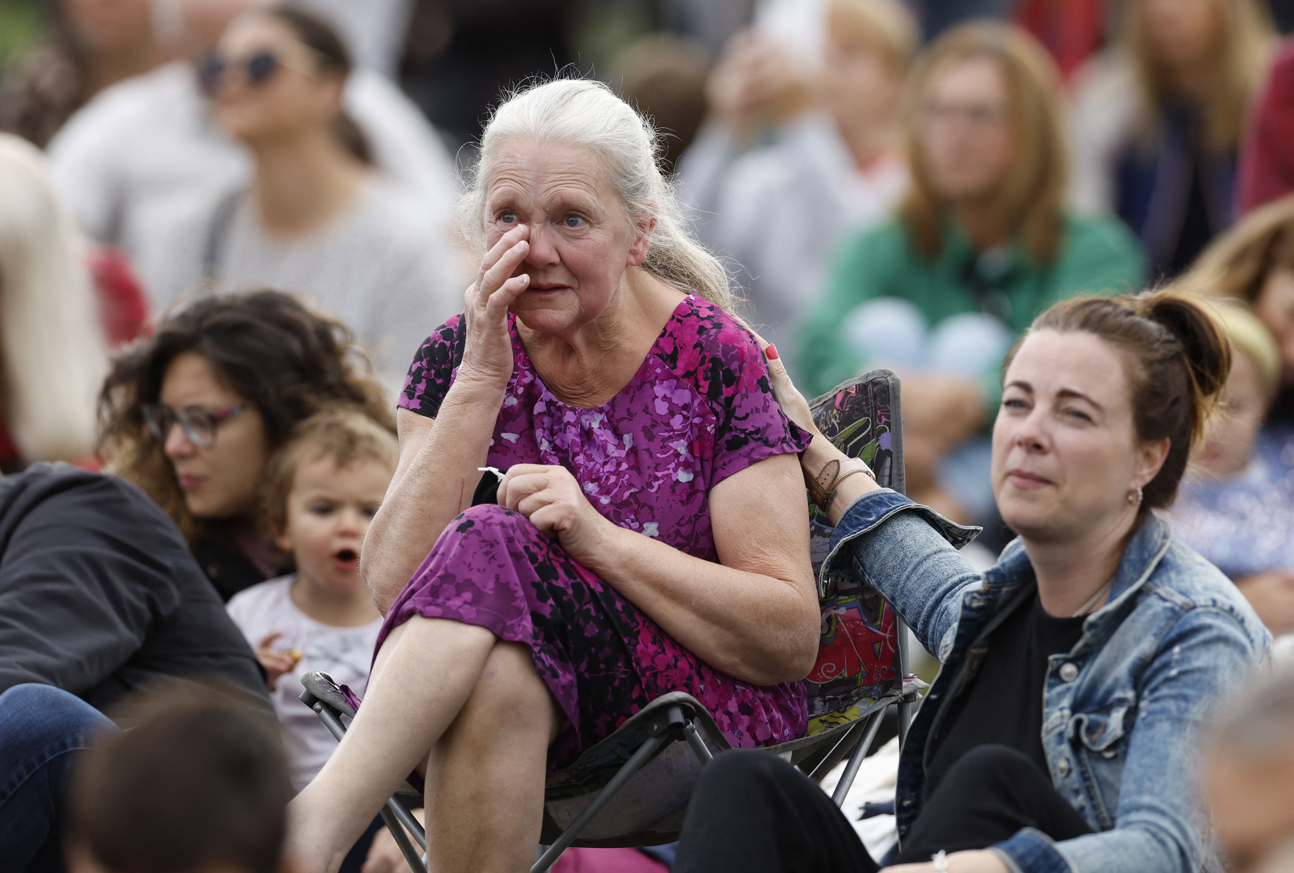 Mujer reacciona mientras la gente se sienta en Hyde Park, para ver el funeral en vivo. 