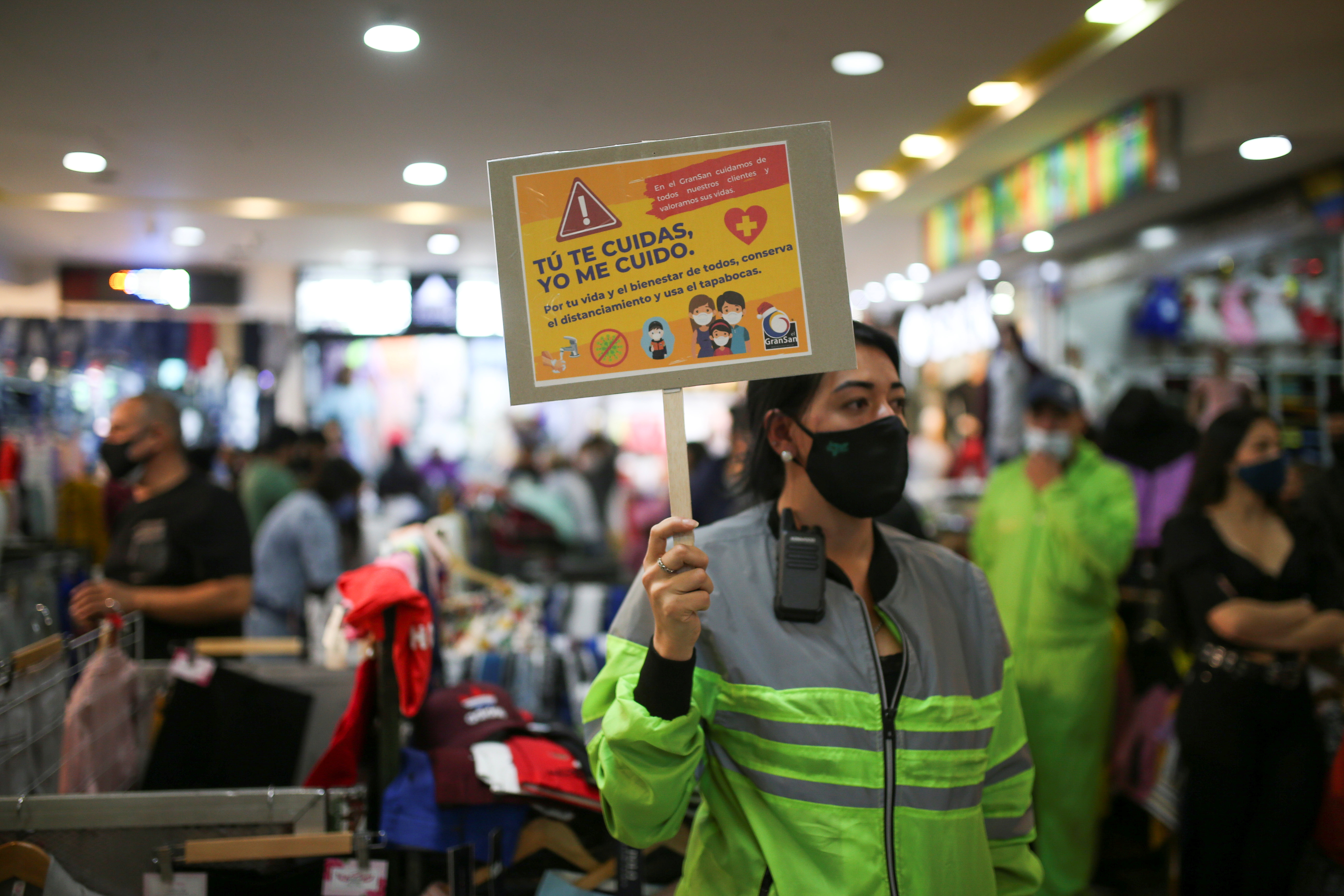 An employee of commercial sector of San Victorino wearing a face mask holds a sign that reads "You take care of yourself, I take care of myself, for your life and the well-being of all keep your distance and wear the face mask" during the Christmas sales season as the coronavirus disease (COVID-19) outbreak continues in Bogota, Colombia December 5, 2020. Picture taken December 5, 2020. REUTERS/Luisa Gonzalez