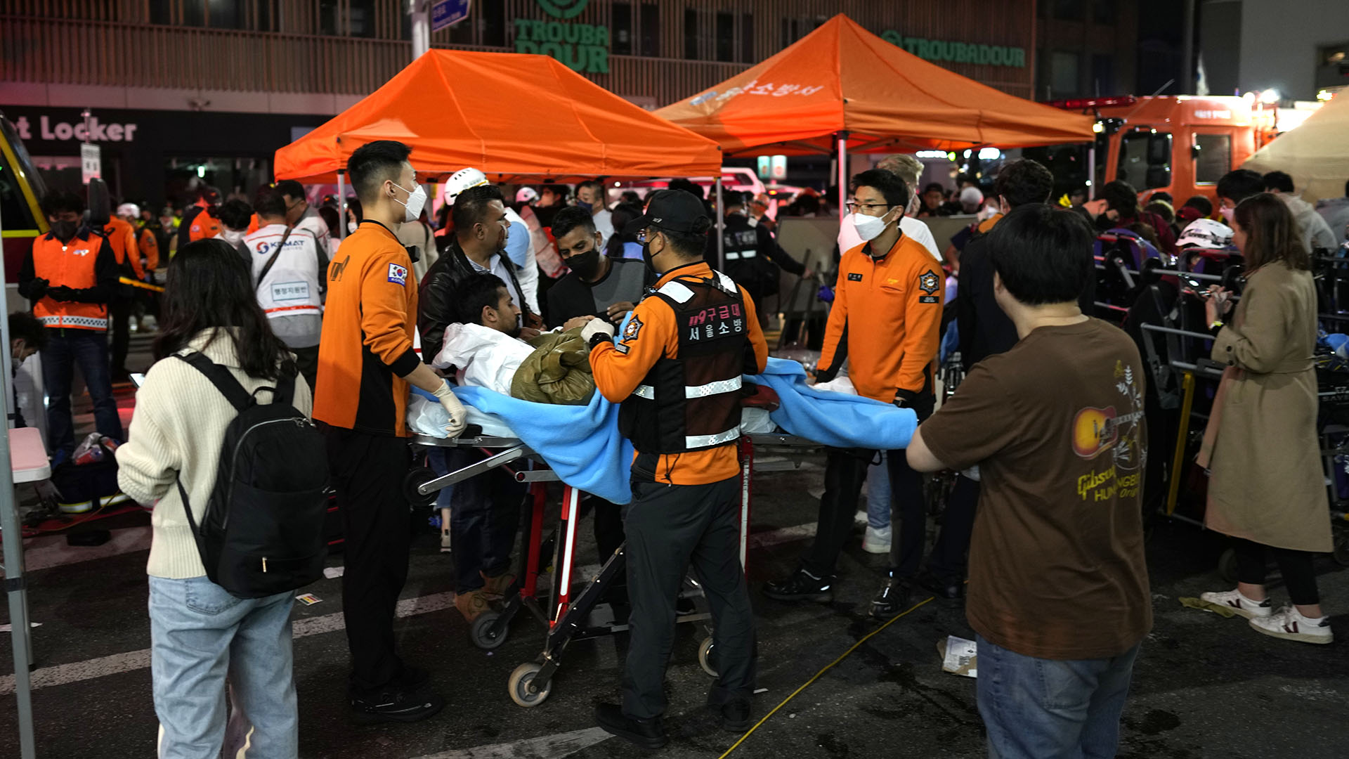 Rescue workers carry injured people at the street near the scene in Seoul, South Korea, early Sunday, Oct. 30, 2022. South Korean officials said around 50 people were in cardiac arrest and a number feared dead after being crushed by a large crowd pushing forward on a narrow street during Halloween festivities in the capital Seoul.  (AP Photo/Lee ​​Jin-man)