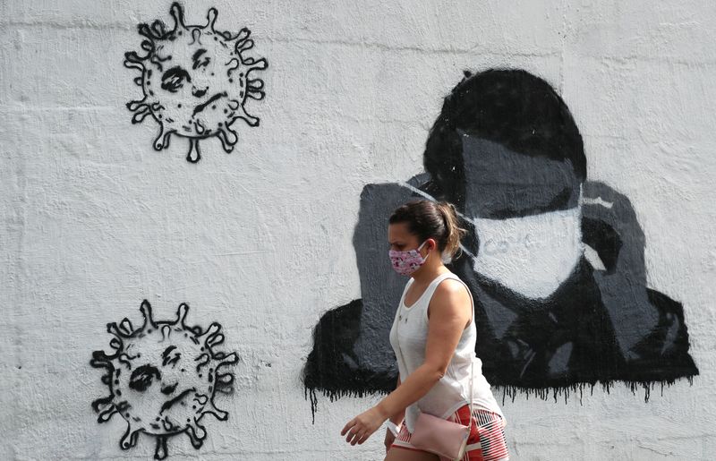 Foto de archivo. Una mujer pasa por delante de un grafiti que muestra al presidente de Brasil, Jair Bolsonaro, ajustando su máscara protectora, en medio del brote de la enfermedad coronavirus (COVID-19) en Río de Janeiro, Brasil. 2 de julio de 2020. REUTERS/Sergio Moraes
