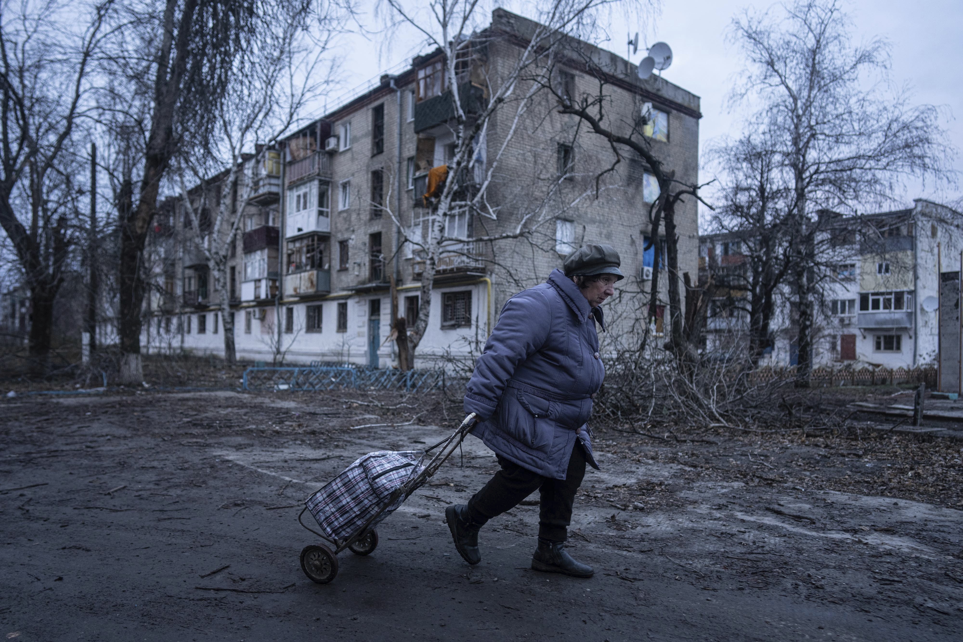 Una mujer camina a un centro de distribución de ayuda humanitaria frente a una vivienda dañada por los ataques rusos en Kupiansk, en la región de Járkiv, Ucrania, el miércoles 26 de diciembre de 2022. (AP Foto/Evgeniy Maloletka)