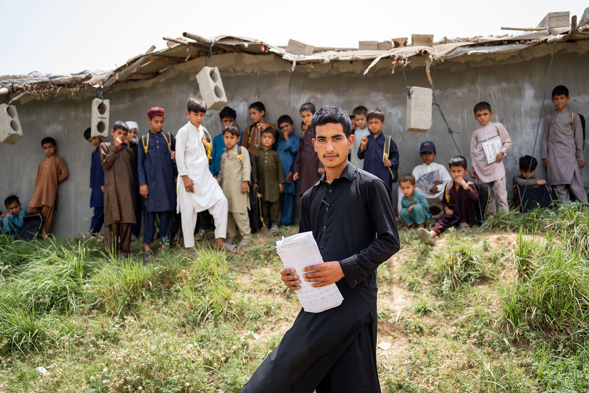 Un maestro de escuela de 19 años se encuentra con su clase frente a una escuela improvisada en un campo de refugiados en las afueras de Islamabad, Pakistán. 