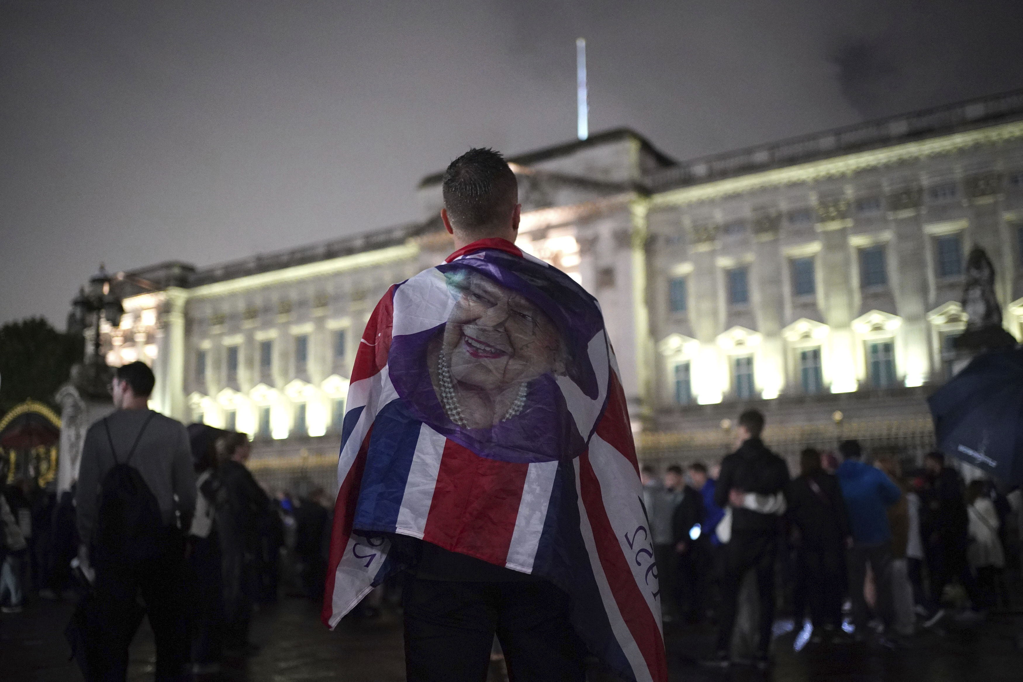 Un joven porta una bandera del Reino Unido con la cara de la reina Isabel II (James Manning/PA via AP)