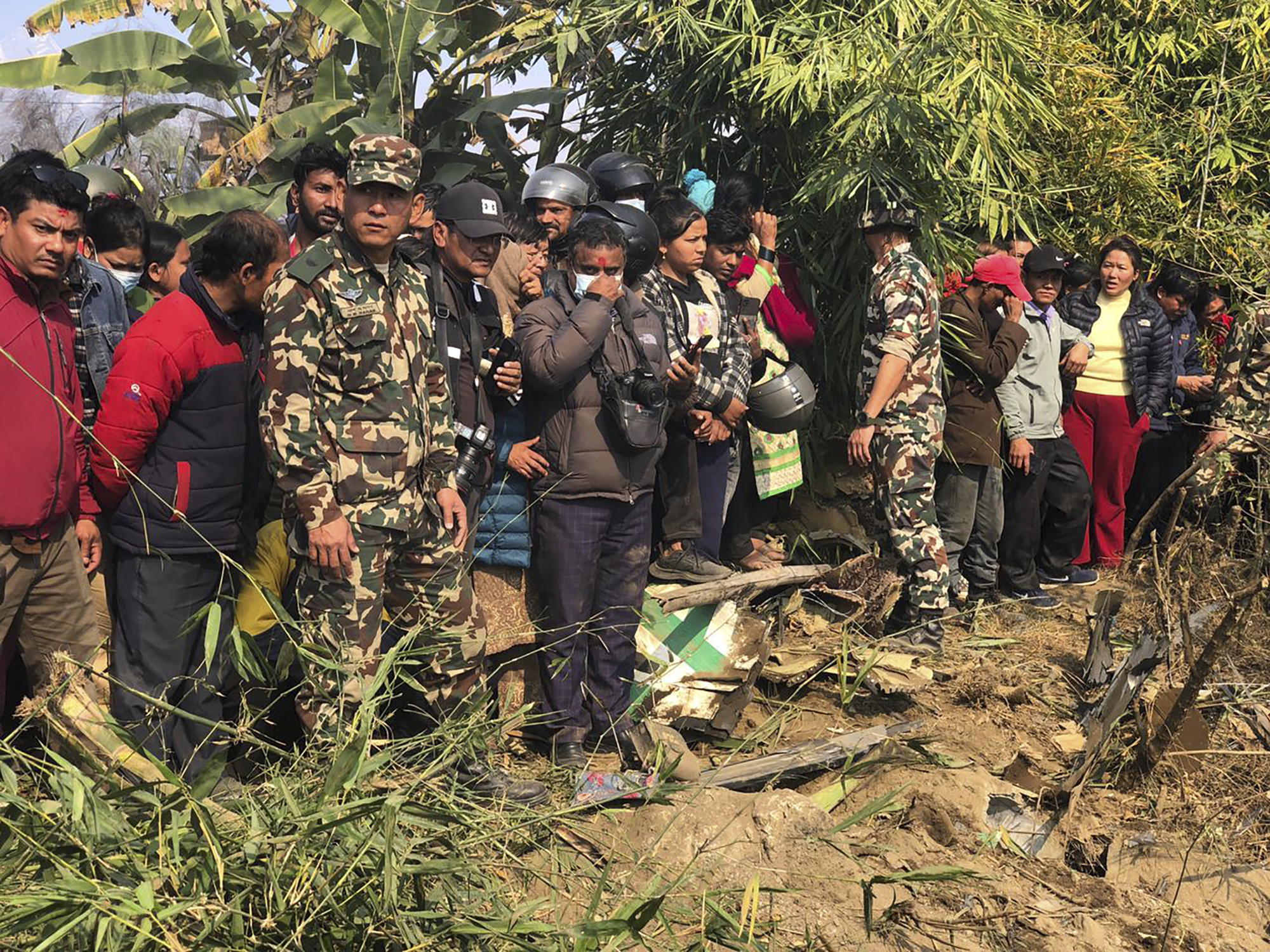 Varias personas observan los restos de un avión de pasajeros accidentado el domingo 15 de enero de 2023, en Pokhara, Nepal. (AP Foto/Ashish Puri)