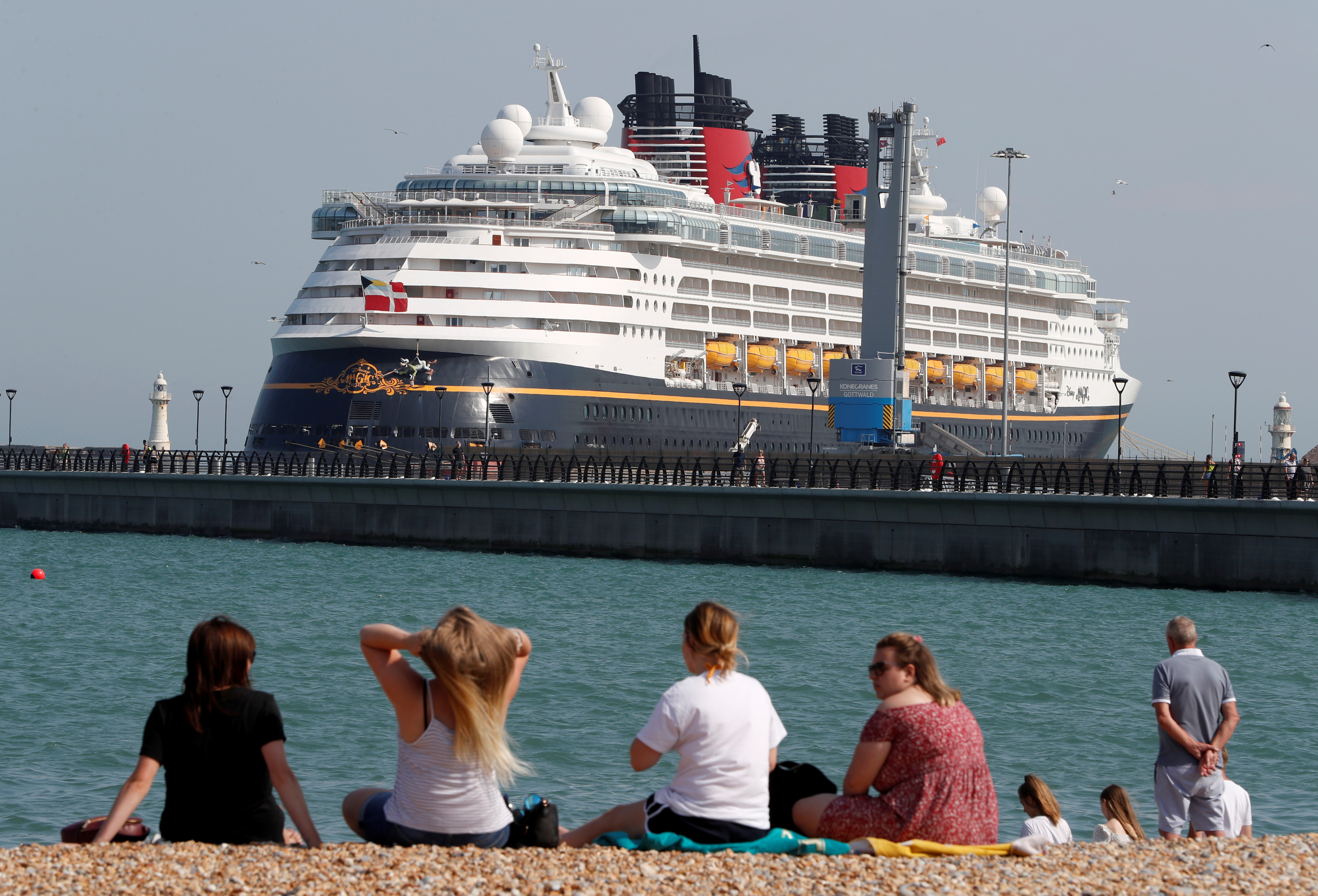 People enjoy the hot weather on the beach as the cruise ship "Disney Magic" ferry is seen docked in the port of Dover, amid the coronavirus disease (COVID-19) outbreak, in Dover, Britain August 9, 2020. REUTERS/Paul Childs