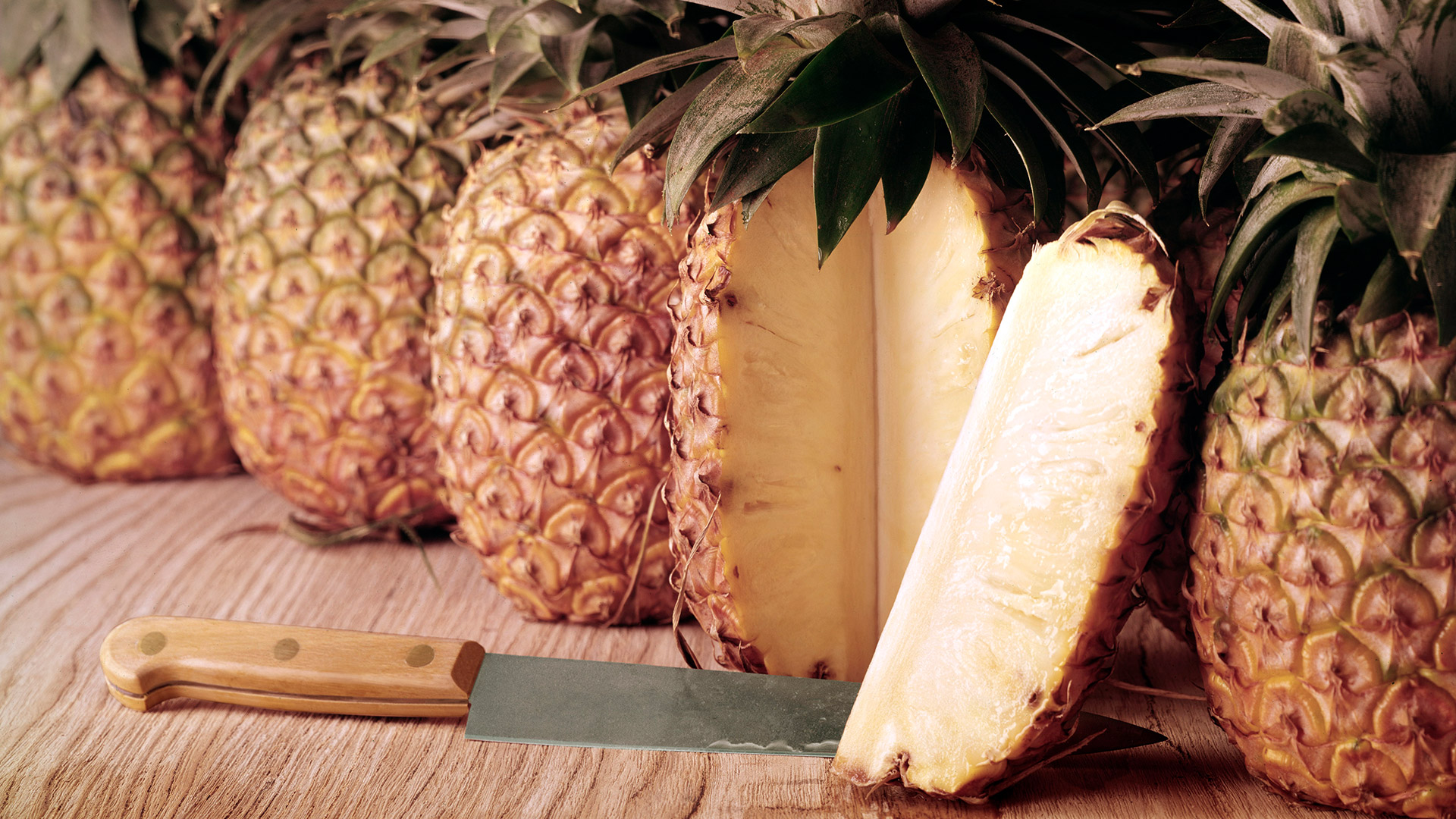 Pineapples with cut pineapple, with a kitchen knife, against a wood background, 2011. (Photo by Tom Kelley/Getty Images)