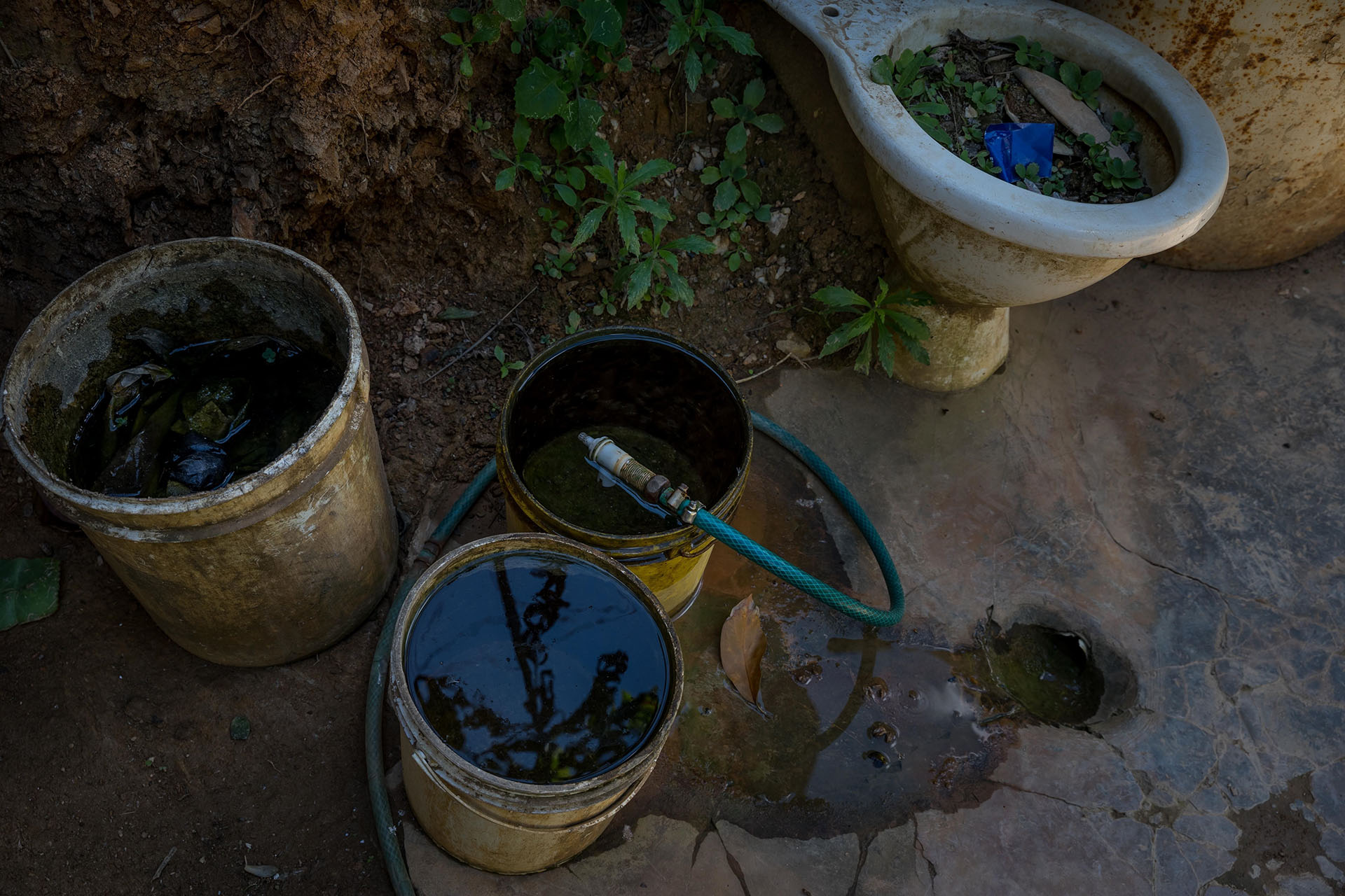 Se observan envases plásticos donde se almacena agua que emana de piedras en una barriada, en Caracas (EFE/ Miguel Gutiérrez)