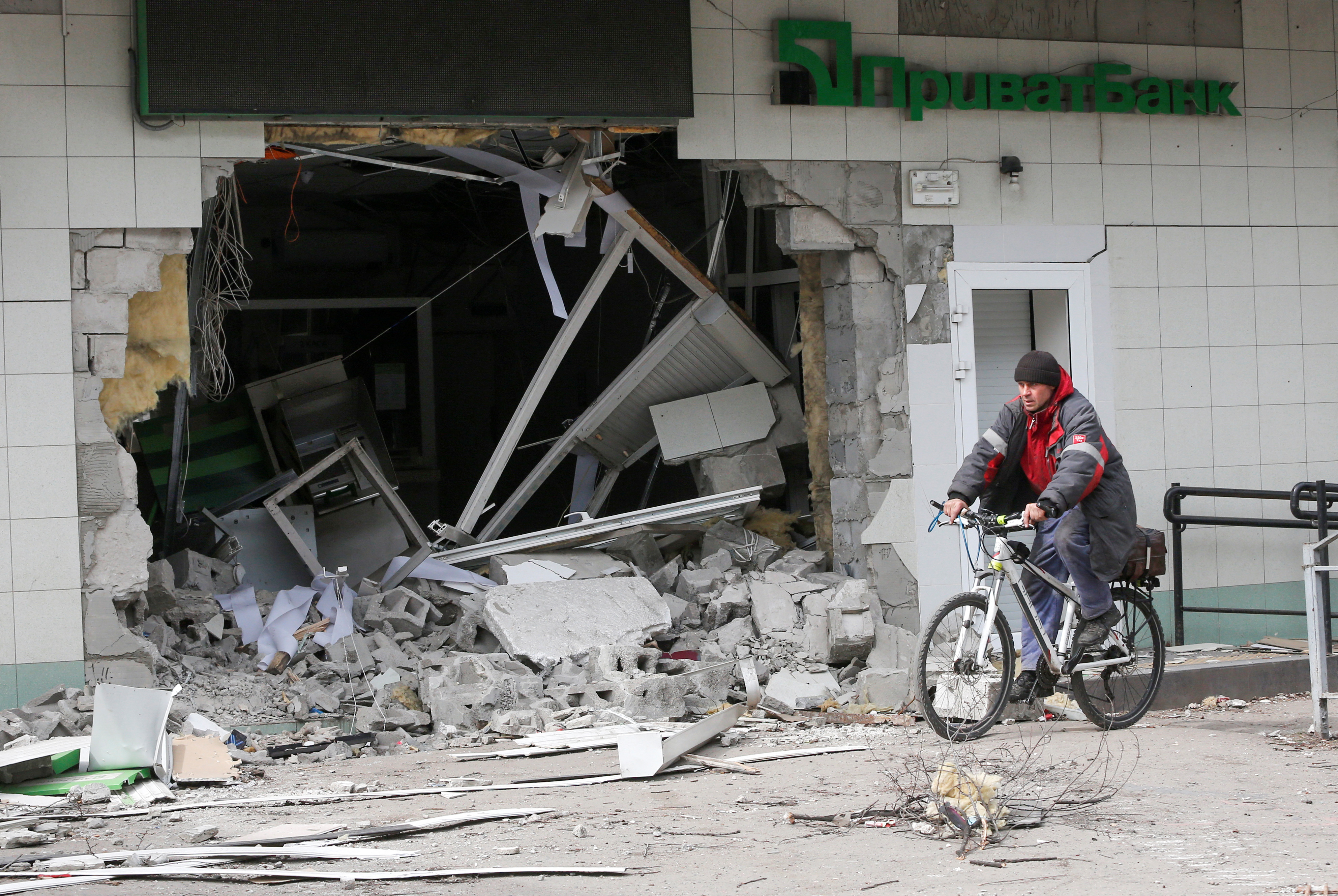 Un hombre monta una bicicleta cerca de una sucursal bancaria dañada por los ataques rusos en Mariupol 