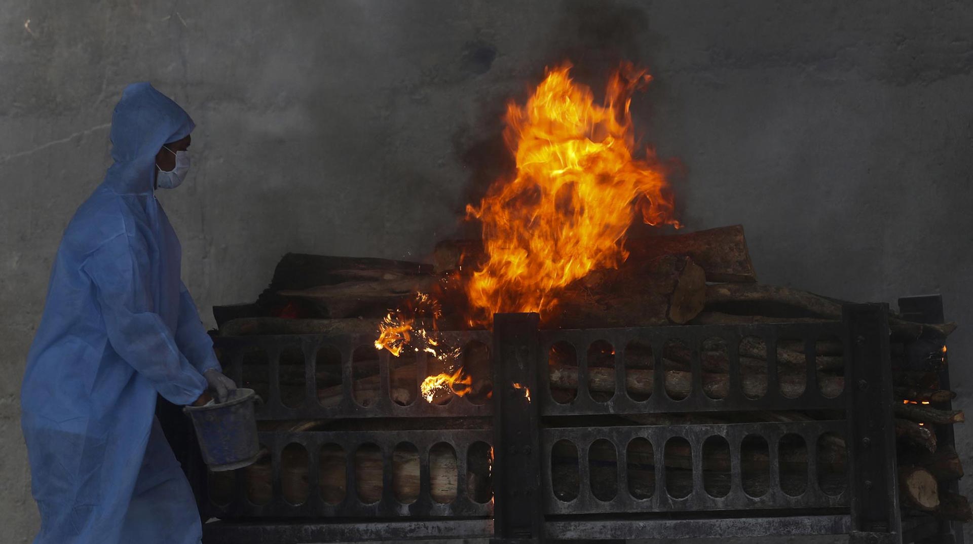 Un trabajador municipal con traje de protección personal realiza los últimos ritos durante la cremación de una víctima de COVID-19 en Vasai, en las afueras de Mumbai, India (AP)