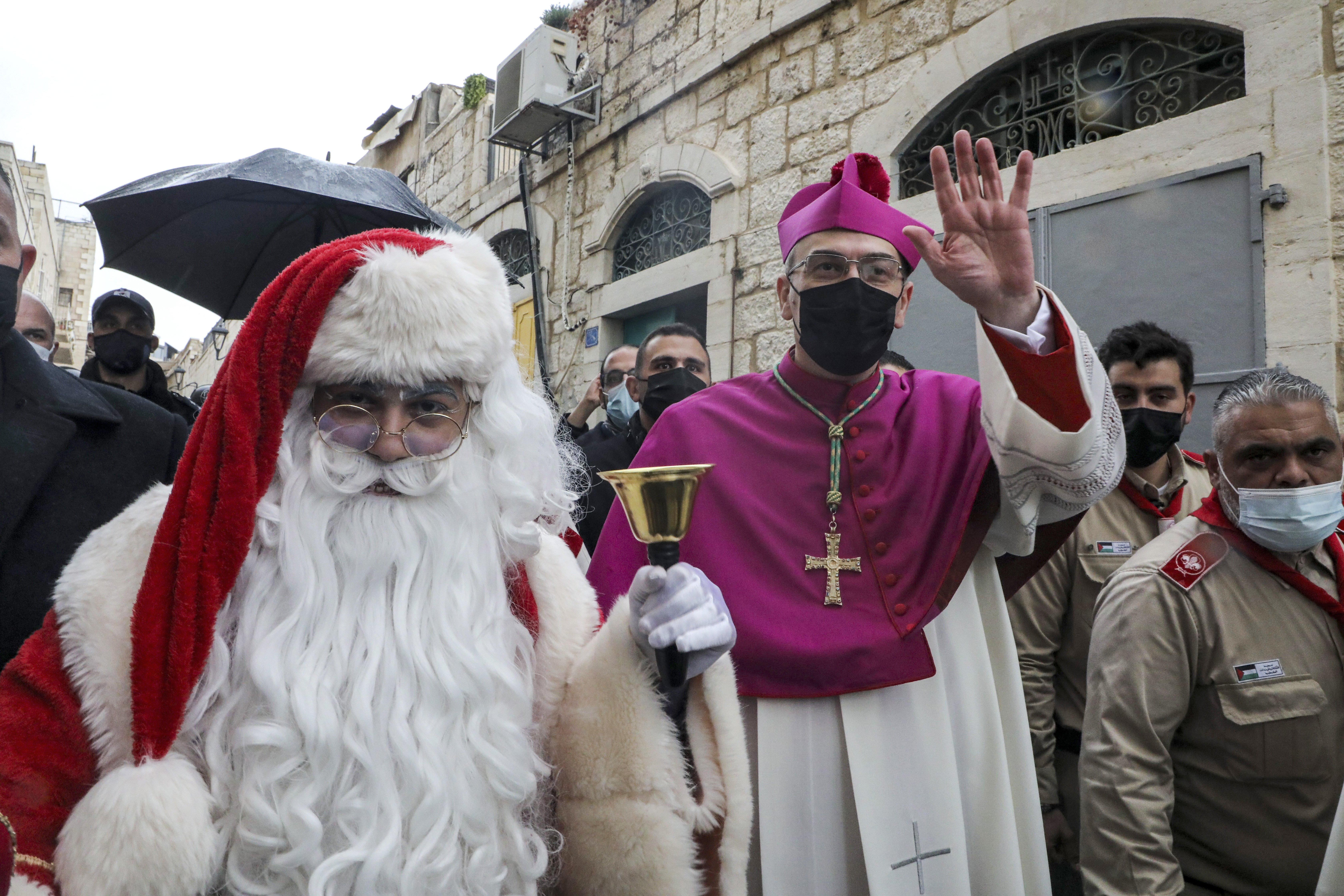 El Arzobispo Pierbattista Pizzaballa, Patriarca Latino de Jerusalén, saluda a la gente mientras camina junto a un hombre vestido como Papá Noel cuando llega para asistir a las celebraciones navideñas en la ciudad bíblica de Belén, en Cisjordania (Foto de HAZEM BADER / AFP)