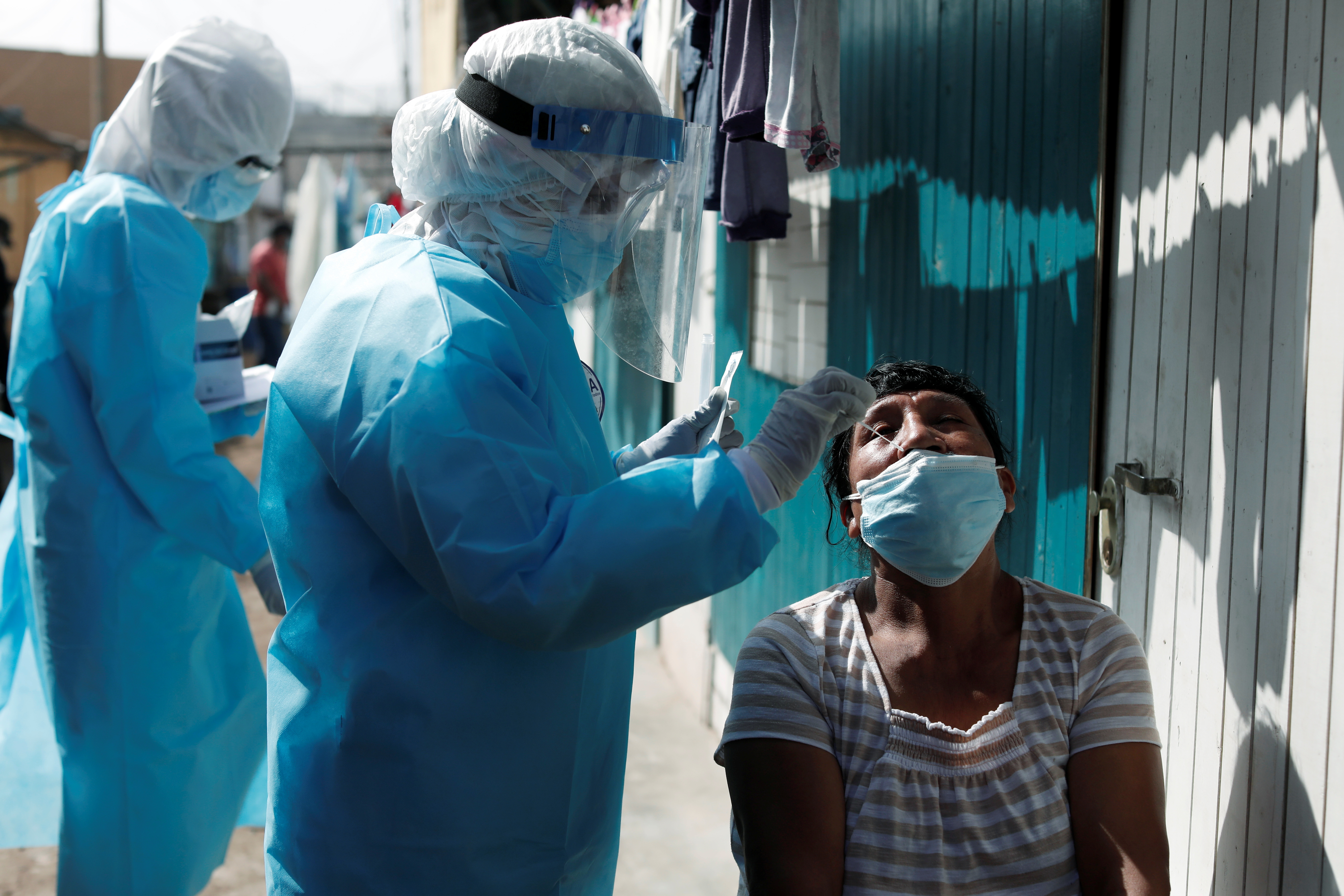A healthcare worker wearing personal protective equipment (PPE) takes a swab sample from a woman for the coronavirus disease (COVID-19) test in Cantagallo, an indigenous Shipibo-Conibo community, during the vaccination campaign against the coronavirus, in Lima, Peru February 19, 2021. REUTERS/Angela Ponce