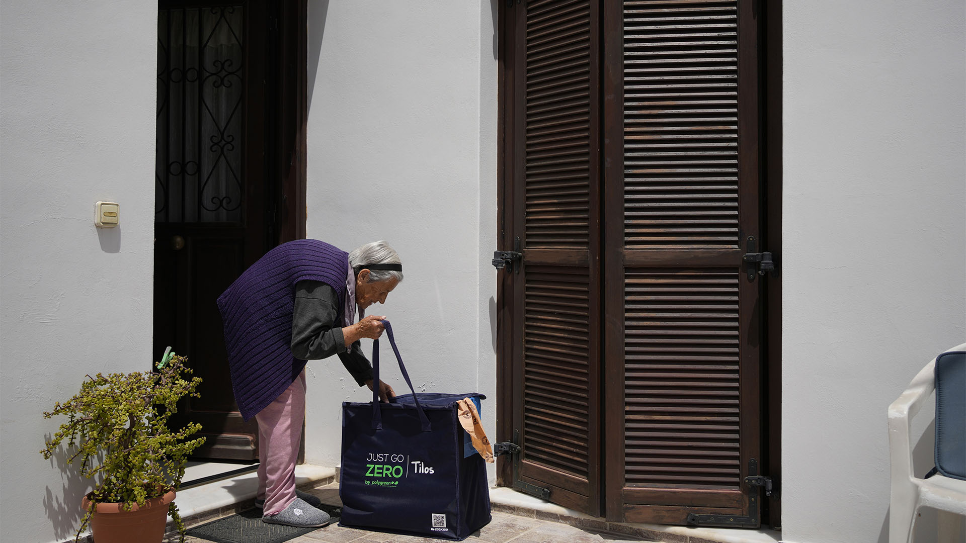 An elderly woman picks up a recycling bag after workers picked up trash from her home (AP Photo/Thanassis Stavrakis)