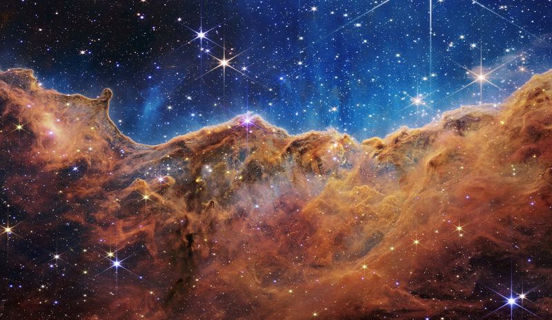 El "acantilado cósmico" de la nebulosa Carina se ve en una imagen dividida horizontalmente por una línea ondulante entre un paisaje de nubes que forma una nebulosa a lo largo de la porción inferior y una porción superior comparativamente clara, con datos del telescopio espacial James Webb (NASA, ESA, CSA, STScI, Webb ERO Production Team/Handout via REUTERS)