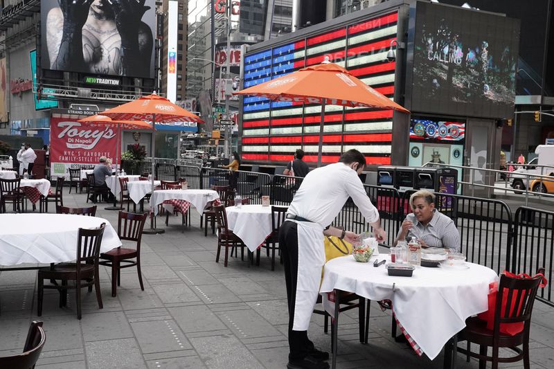 A waiter serves a customer at an outdoor table at an established restaurant in Times Square, New York.
