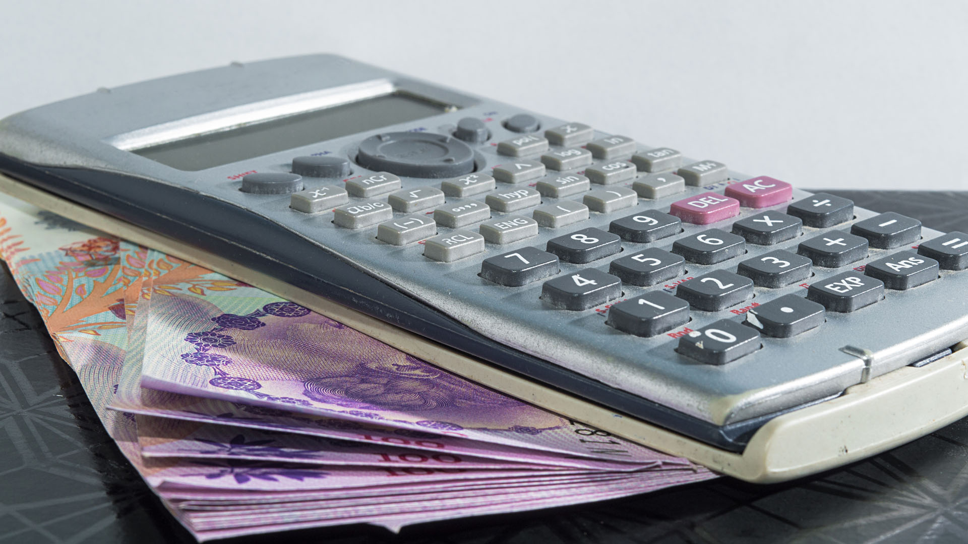 Objeto de oficina, una calculadora un poco deteriorada por el uso, con unos billetes de cien pesos argentinos