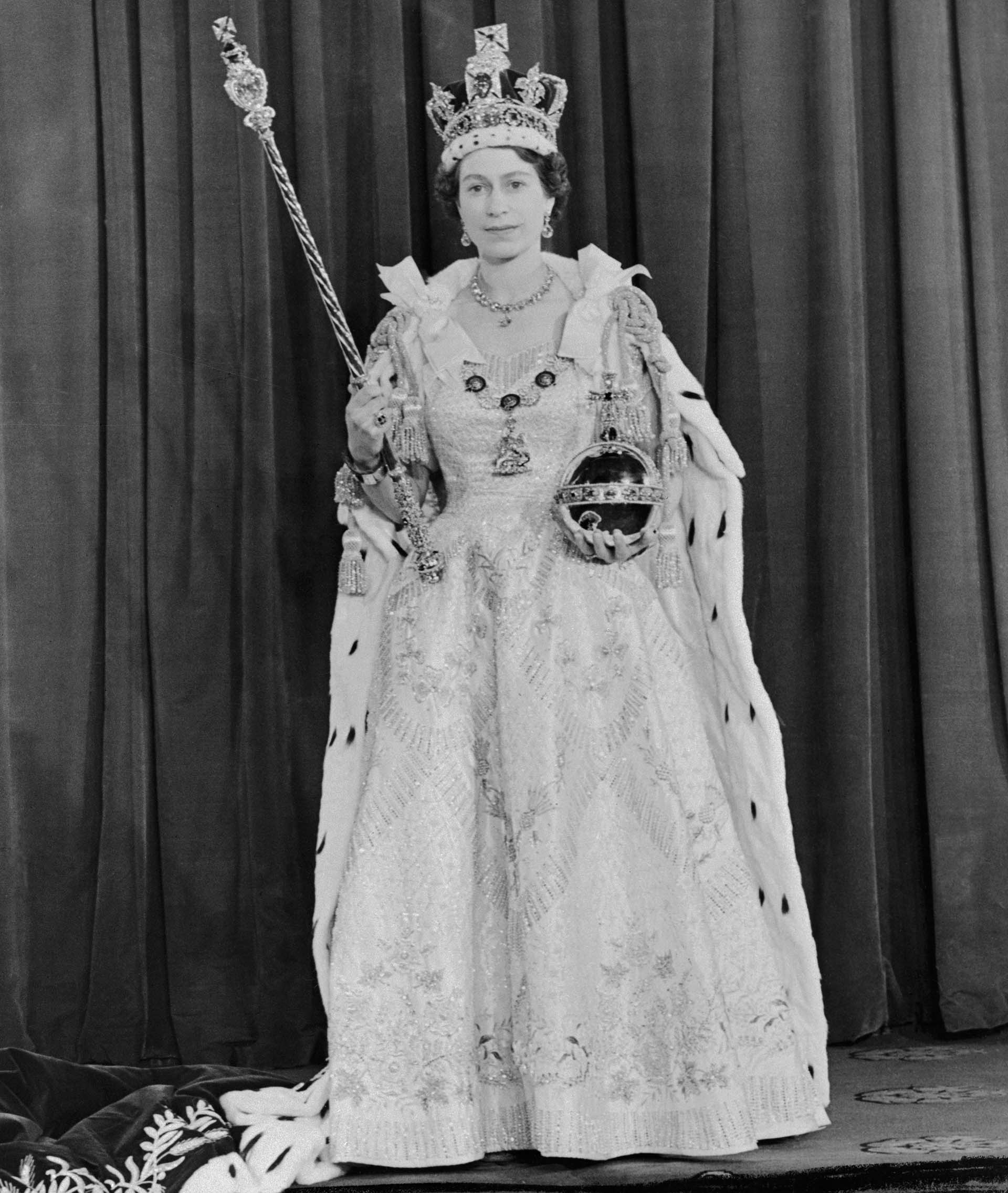 La fotografía oficial de Isabel II el día de su coronación, luciendo todos los símbolos de su poder: la corona imperial, el cetro, el orbe y el anillo imperial. Se diseñaron nueve vestidos, que llevaron meses de trabajo de varias costureras bajo las órdenes de Norman Hartnell, hasta que la monarca se decidió por el octavo modelo