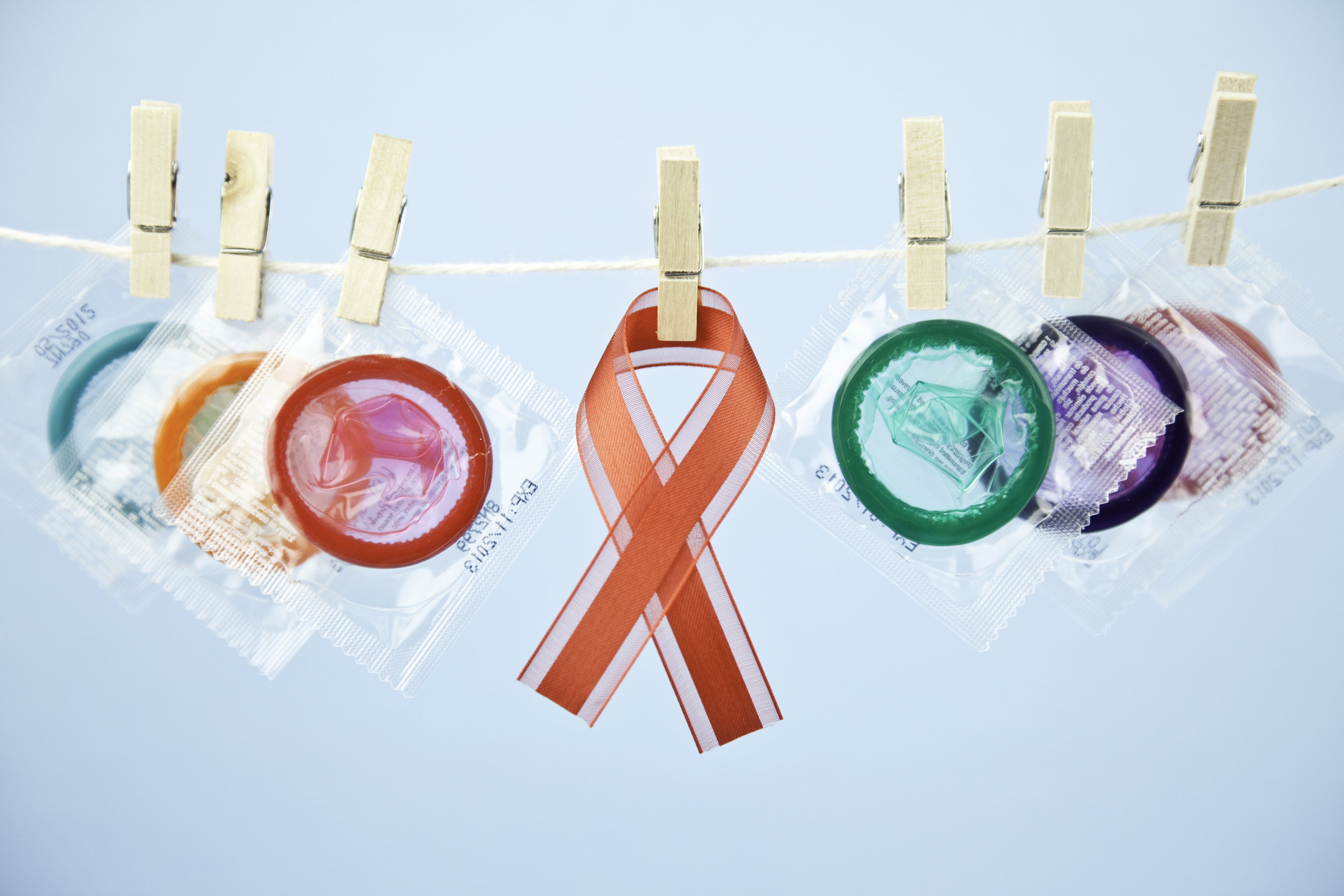 Arrangement of colorful condoms pegged to washing line with AIDS awareness ribbon, as a reminder that safe sex helps prevent the spread of AIDS.