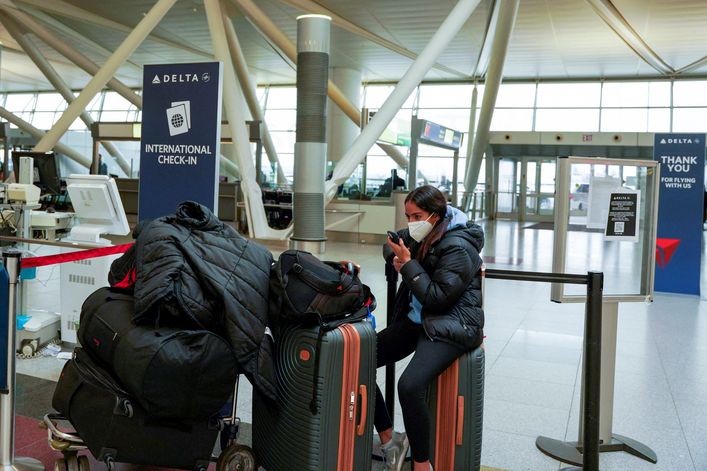 Una pasajera se sienta con su equipaje en el aeropuerto internacional John F. Kennedy después de que las aerolíneas anunciaran la cancelación de numerosos vuelos durante la propagación de la variante del coronavirus Omicron, en Nueva York, Estados Unidos (REUTERS/Dieu-Nalio Chery)