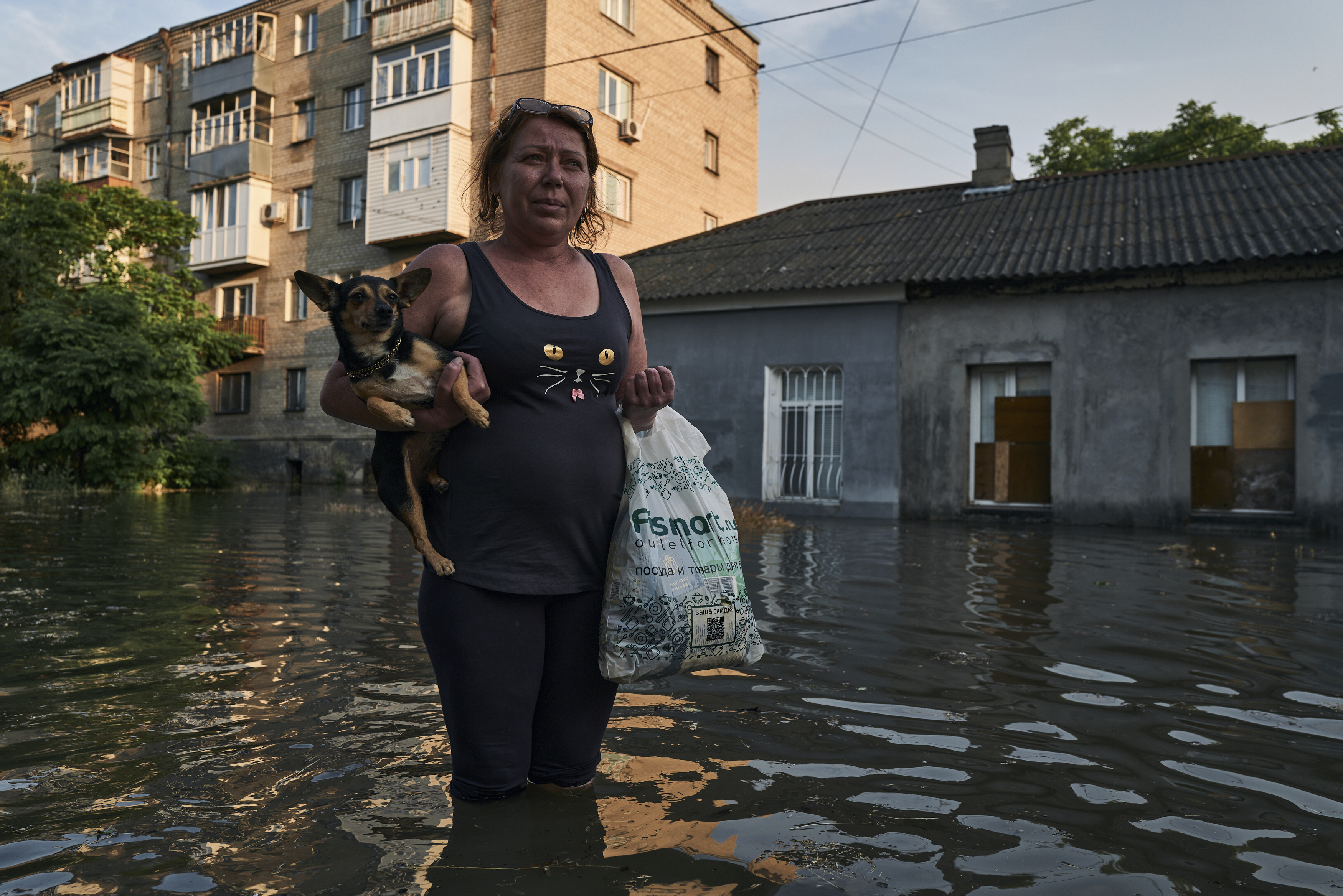 Una mujer camina por una calle inundada en Jersón llevando consigo a su mascota y las pocas pertenencias que puede cargar.