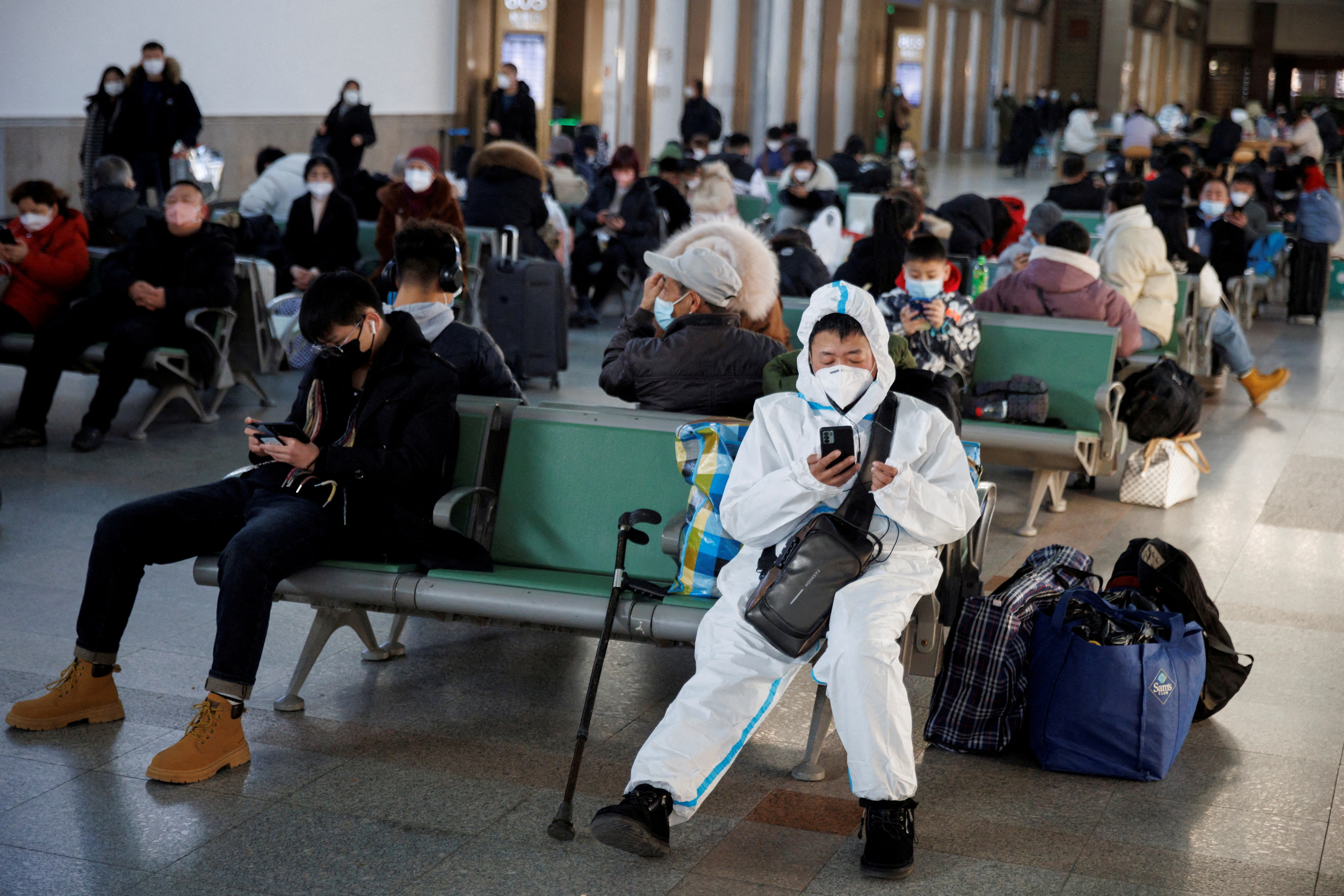 Una persona con un traje protector se sienta en la estación de trenes de Beijing después de que China levantó sus restricciones de COVID-19 en Beijing