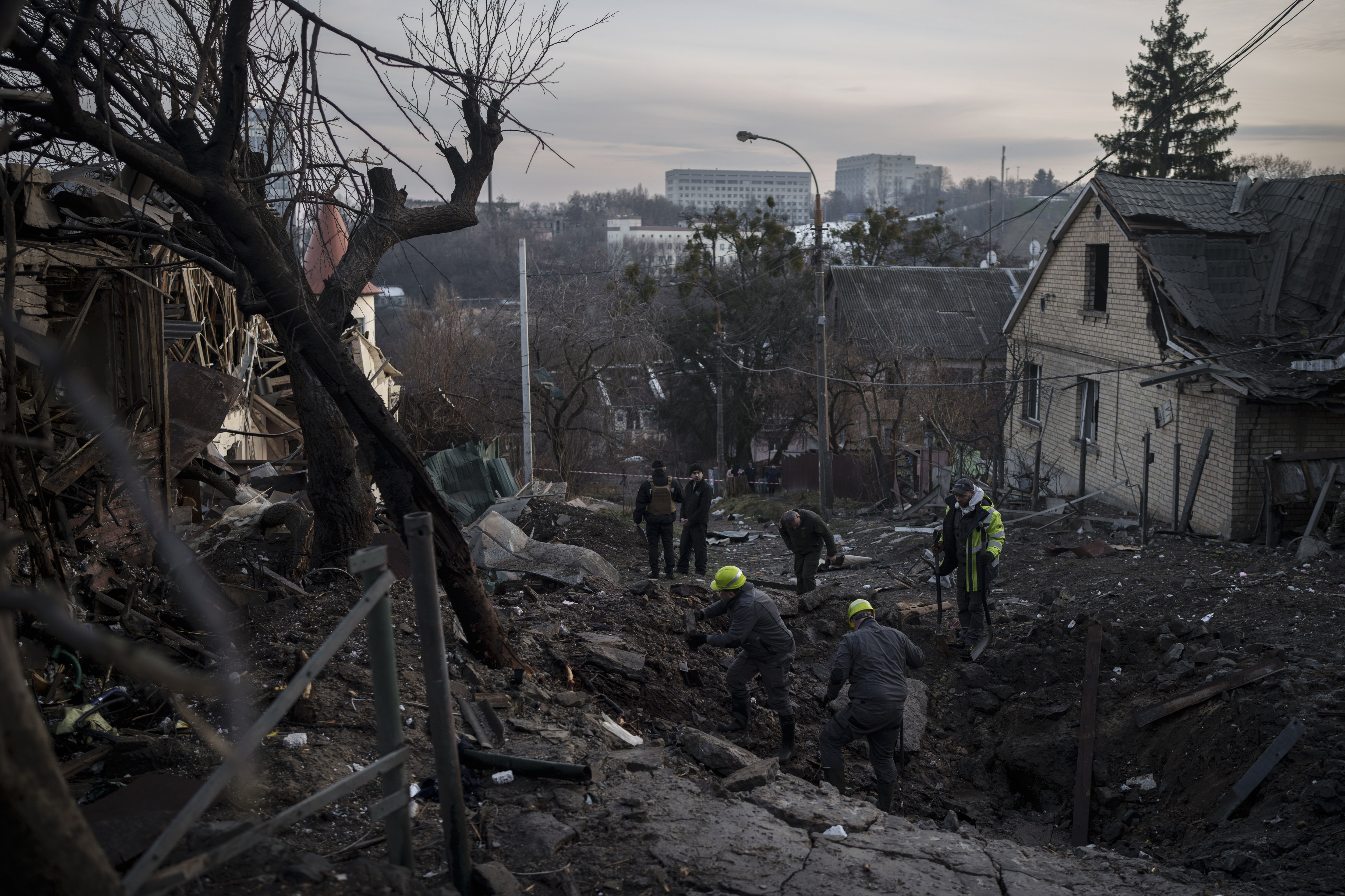 Trabajadores inspeccionan un socavón en una calle residencial después de un ataque ruso el sábado 31 de diciembre de 2022, en Kiev, Ucrania. (AP Foto/Felipe Dana)