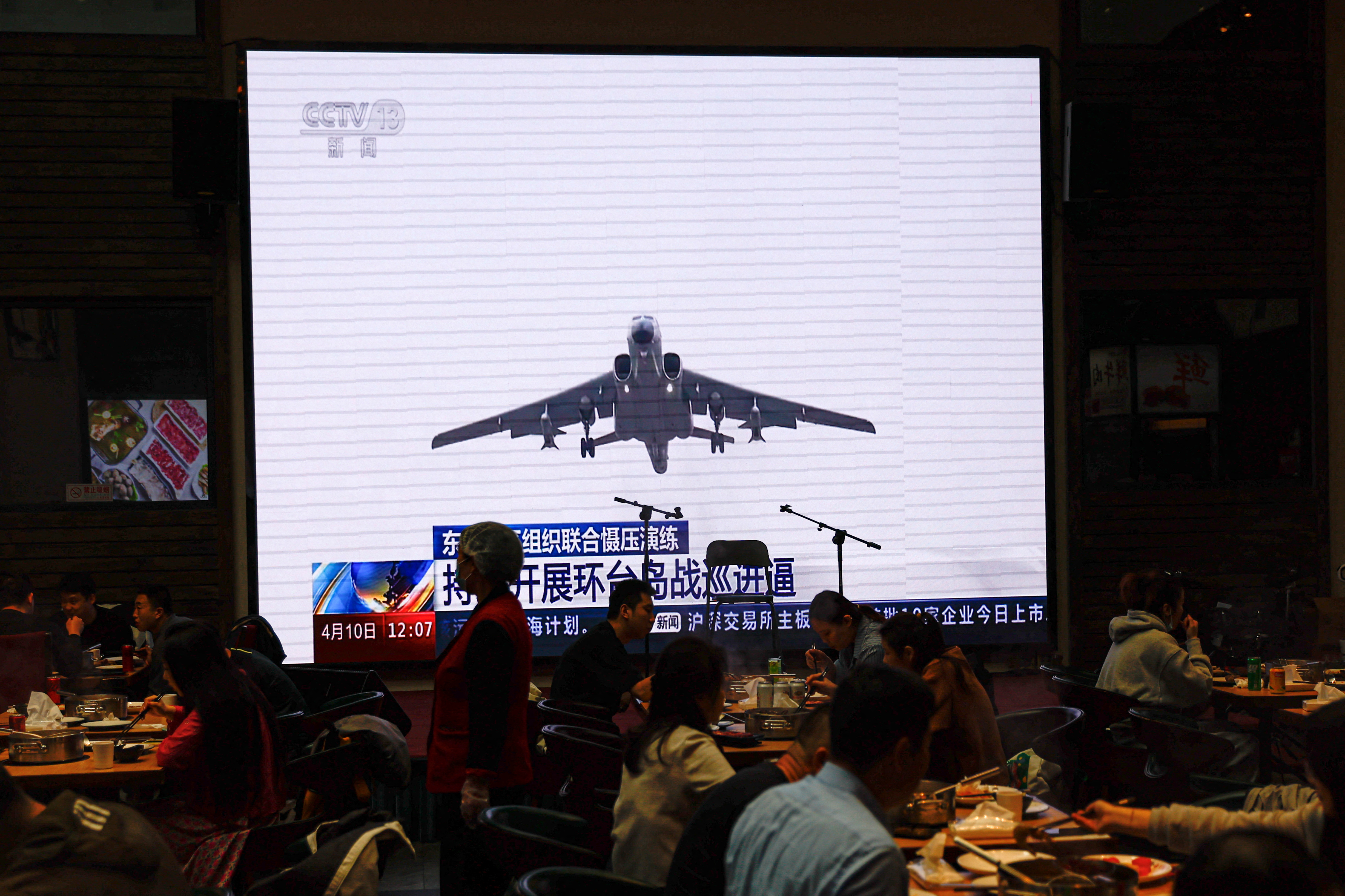 Los clientes cenan cerca de una pantalla gigante que transmite imágenes de noticias de aviones de la Fuerza Aérea bajo el Comando de Teatro del Este del Ejército Popular de Liberación de China (EPL) que participan en una patrulla de preparación para el combate y ejercicios de "Espada Conjunta" alrededor de Taiwán, en un restaurante en Beijing, China 10 de abril de 2023. REUTERS/Tingshu Wang
