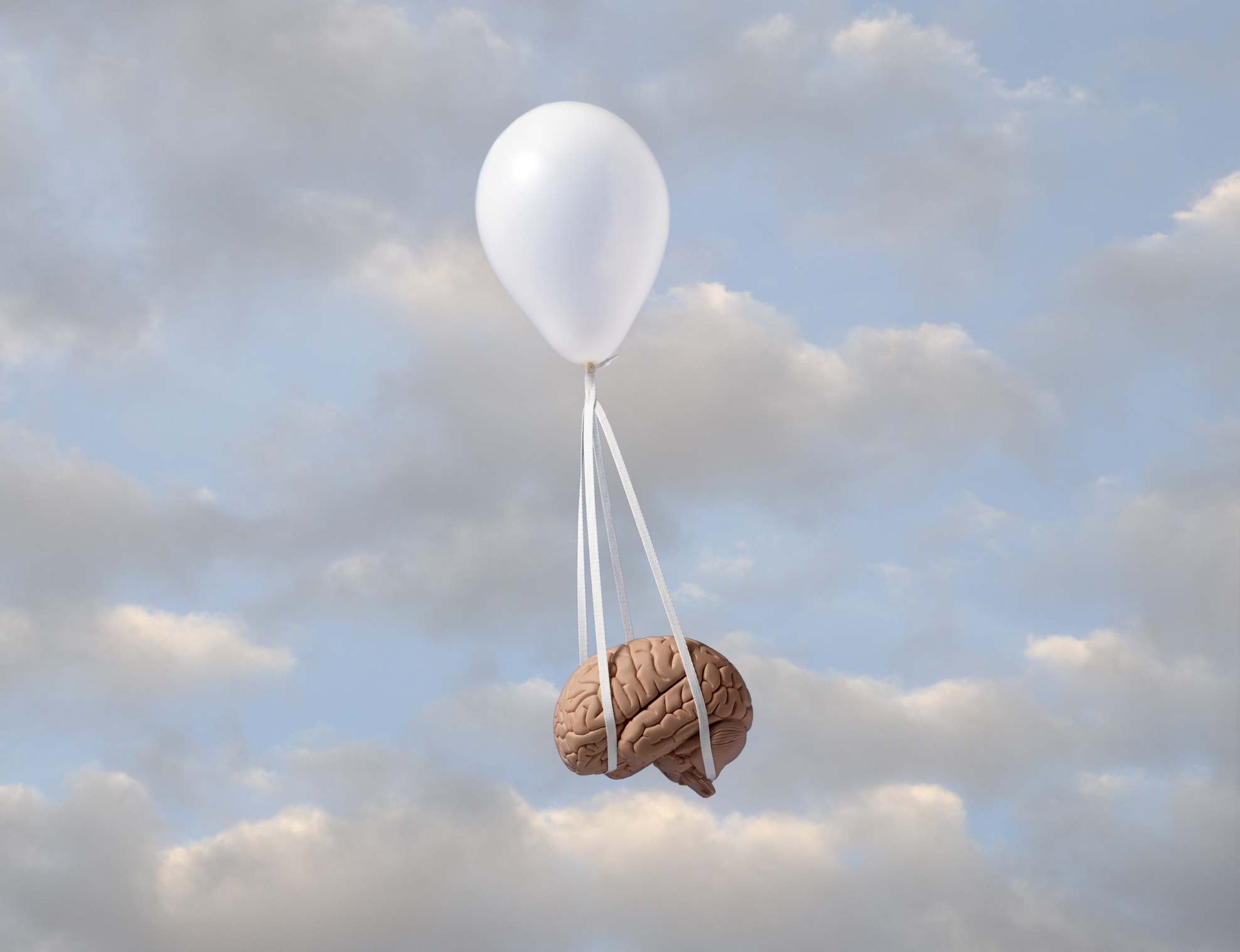 White helium balloon carrying model of human brain with white strings against partly cloudy sky