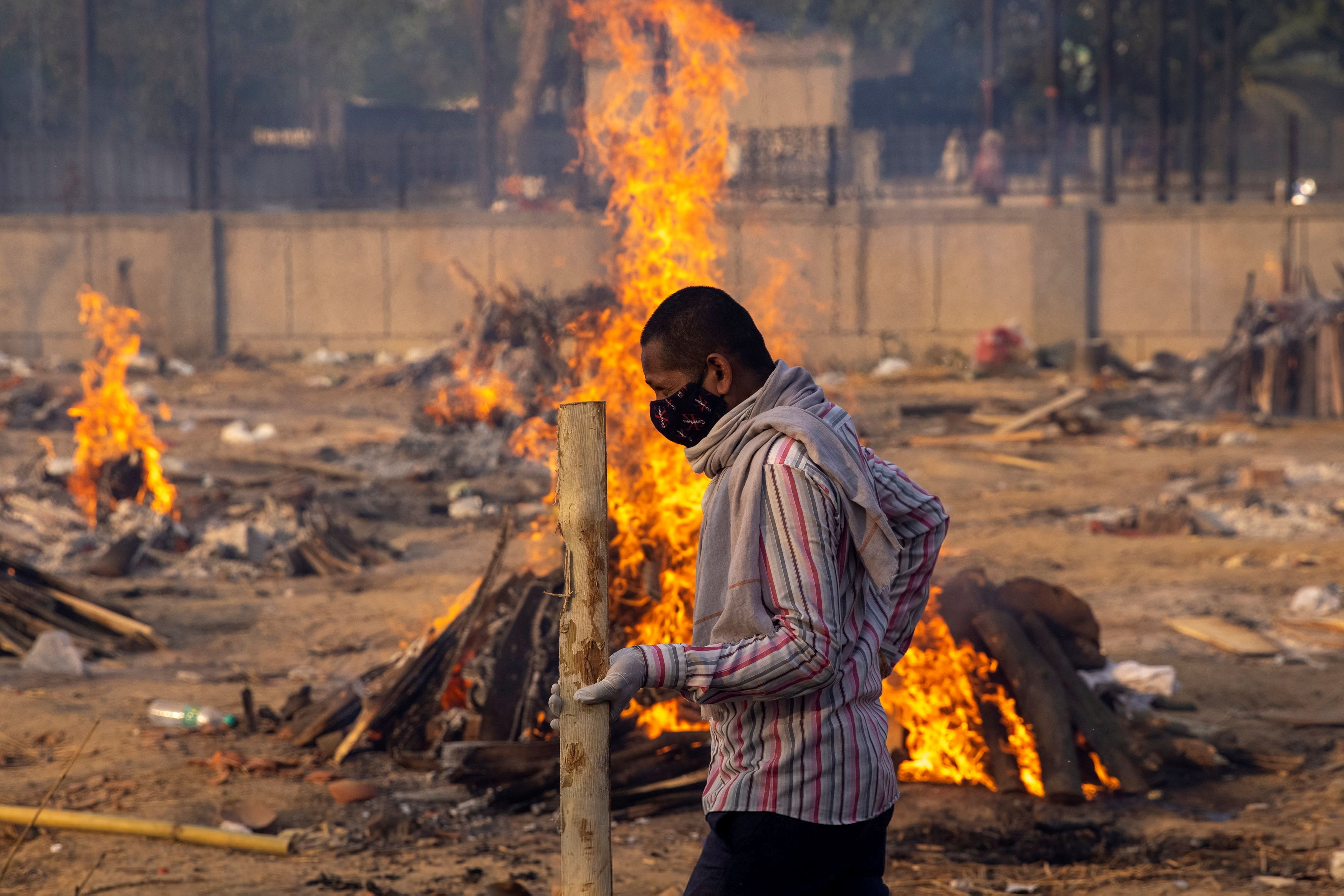 Un hombre pasa junto a piras funerarias en llamas de personas que murieron debido al coronavirus en un crematorio en Nueva Delhi, capital de India (Reuters)