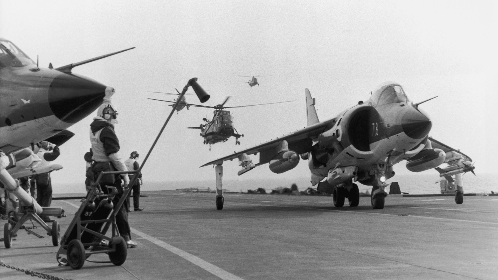 En primer plano un jet Sea Harrier en la cubierta de vuelo del HMS Hermes. De fondo vuelan dos helicópteros Sea King (Martin Cleaver/Pool/Getty Images)