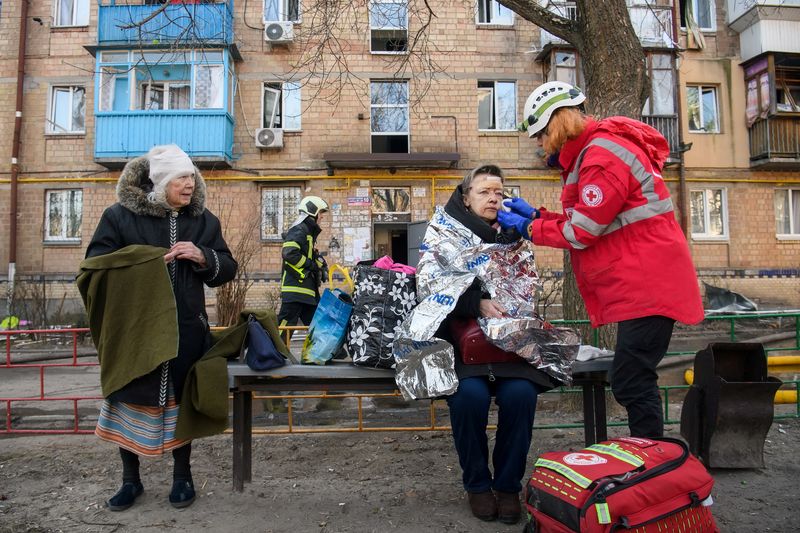 Un paramédico ayuda a una mujer herida en el sitio de un distrito residencial de Kiev después de que fue alcanzado por los bombardeos, mientras la invasión rusa de Ucrania continúa, en Kiev