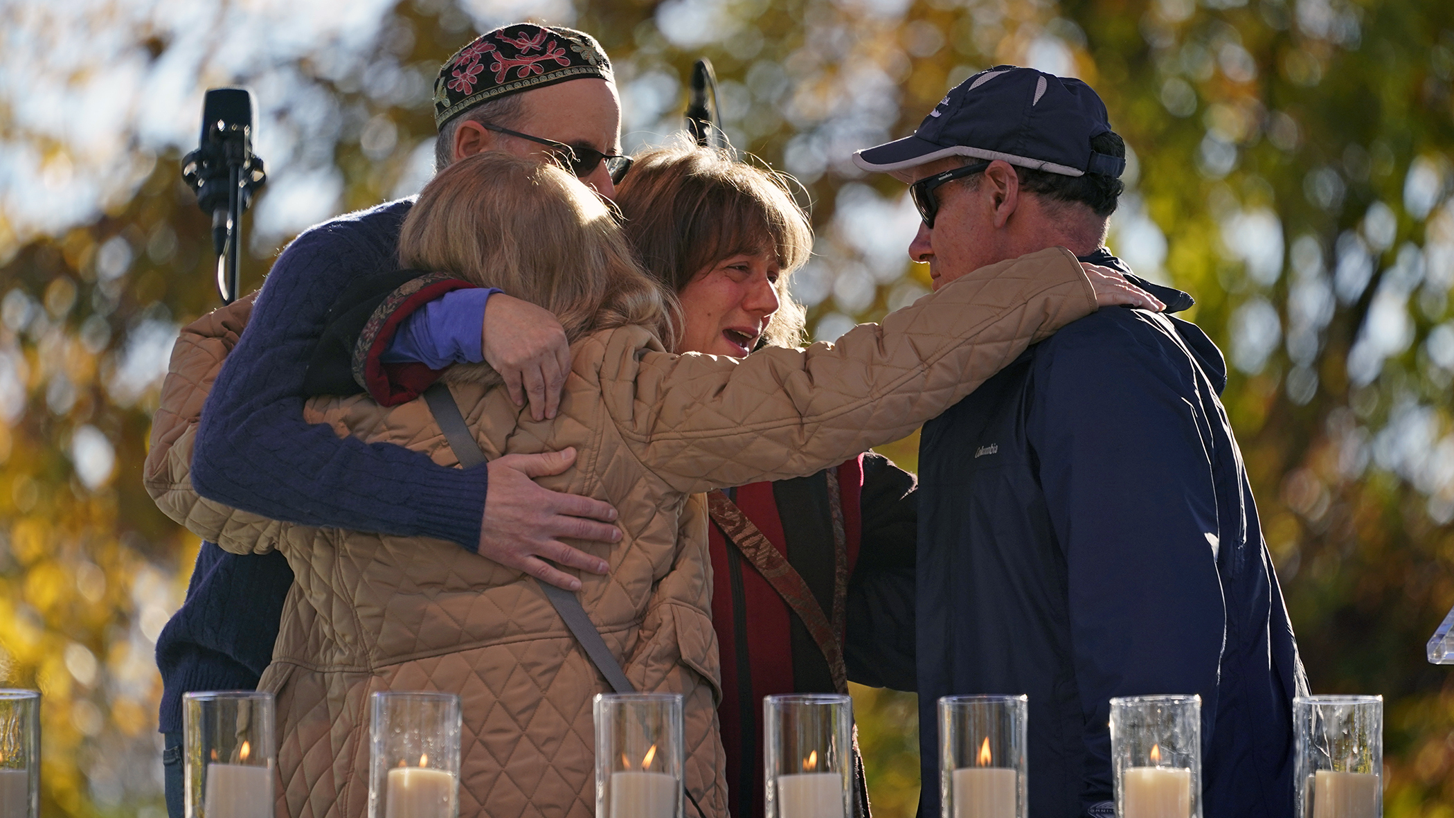 Un grupo de personas se abraza tras encender una vela en memoria de Melvin Wax, uno de los 11 fieles asesinados, durante una ceremonia conmemorativa en Pittsburgh el 27 de octubre de 2022. (AP /Gene J. Puskar)